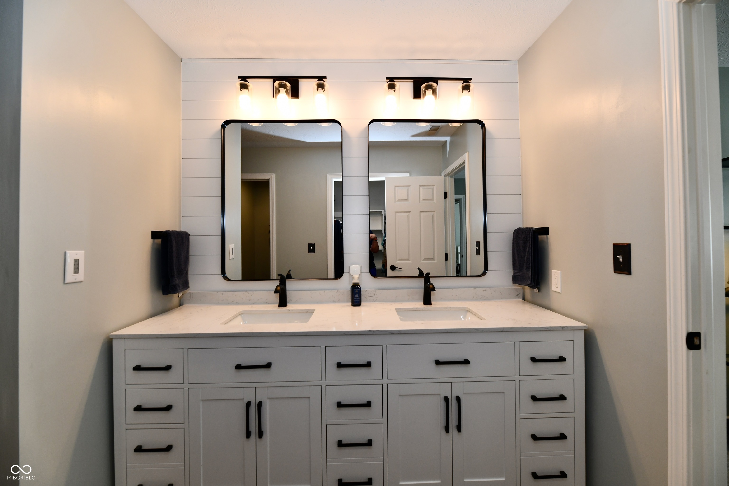 Bathroom with a white double vanity, black fixtures, and two mirrors against shiplap.