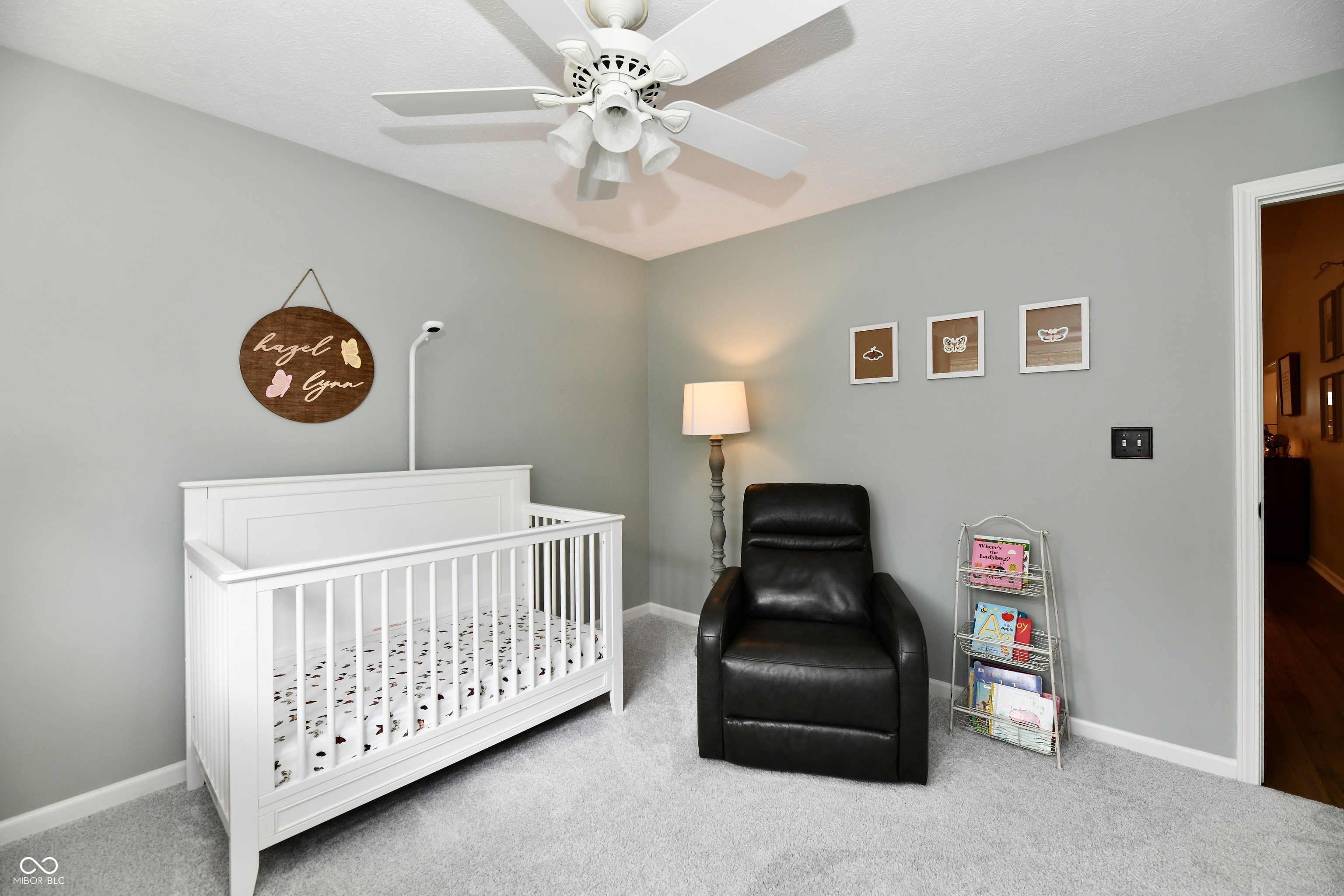 Nursery with a white crib, black leather rocking chair, and round wooden name sign.