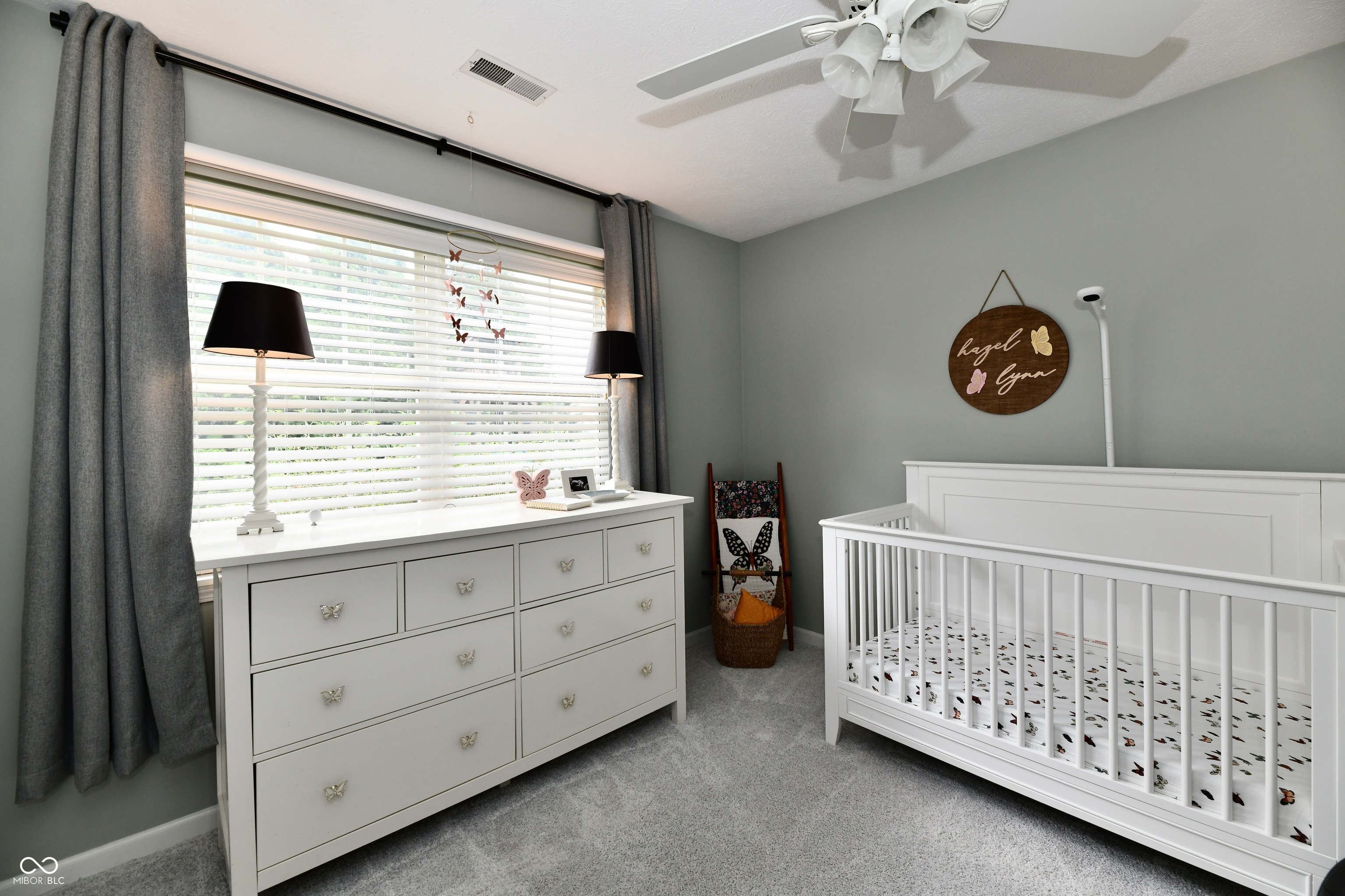 Nursery with a white crib, butterfly bedding, and a dresser beneath a large window.