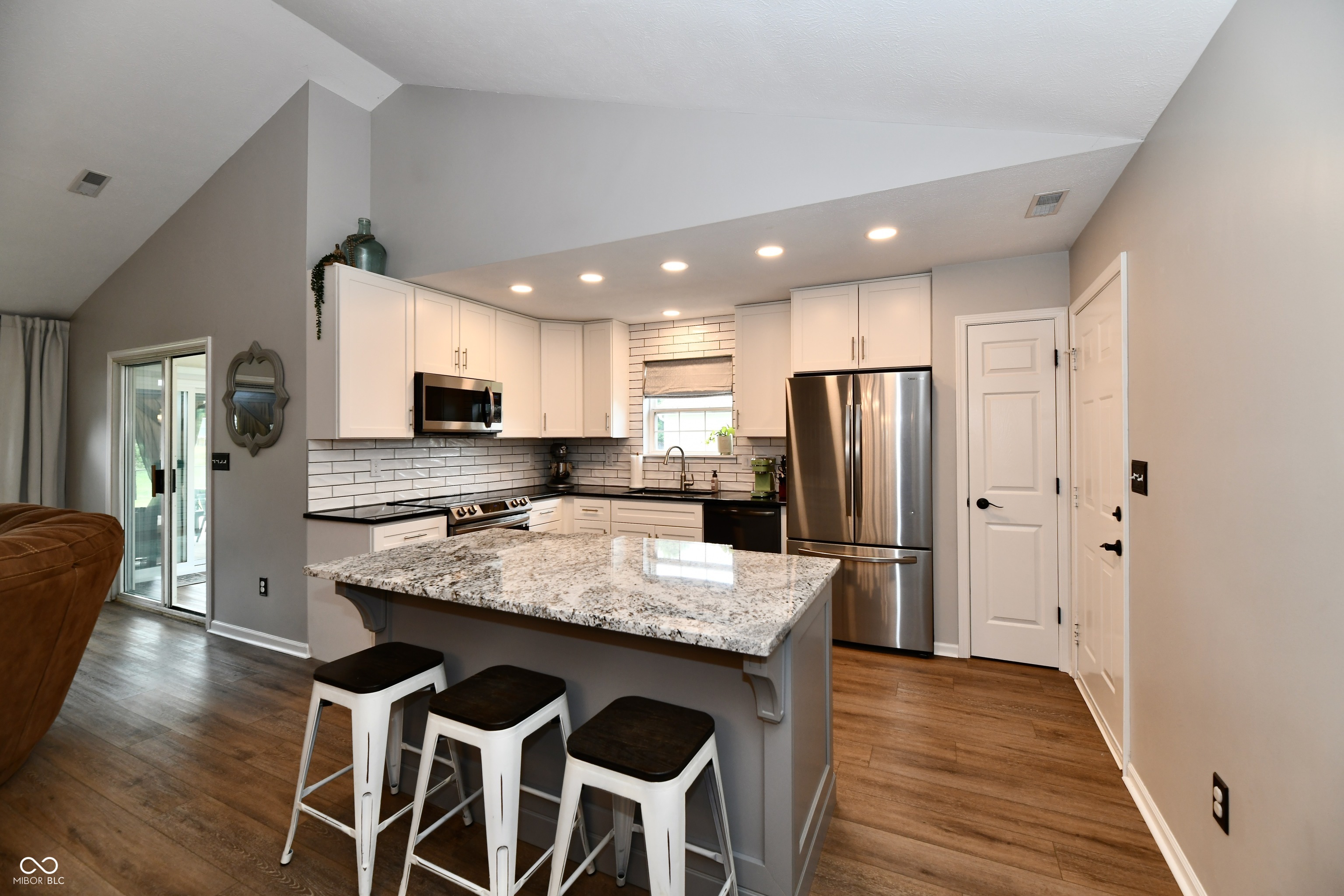Kitchen with white cabinets, stainless steel appliances, and a granite island with three stools.