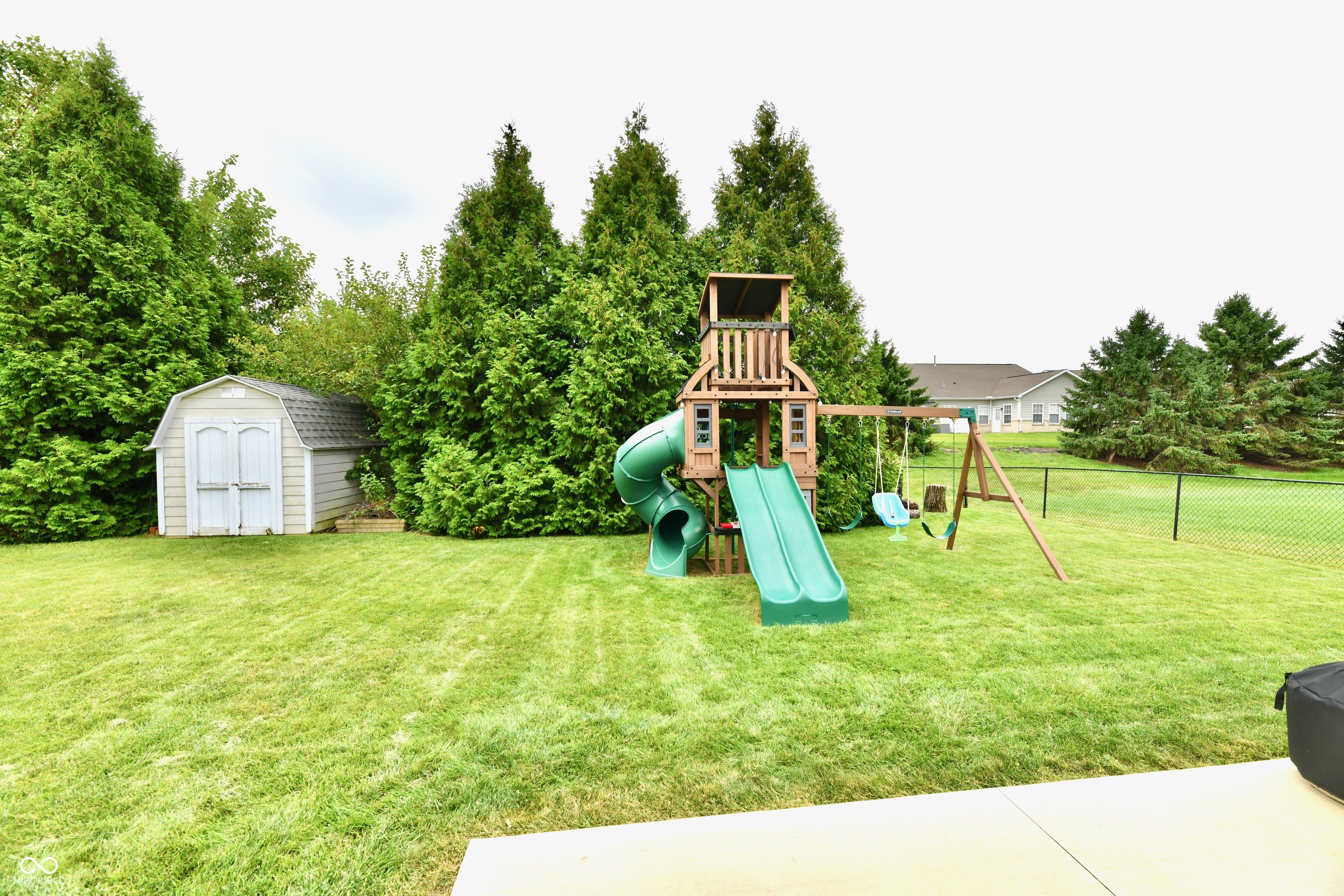 Backyard with a wooden playset, green slides, swings, and a white storage shed.