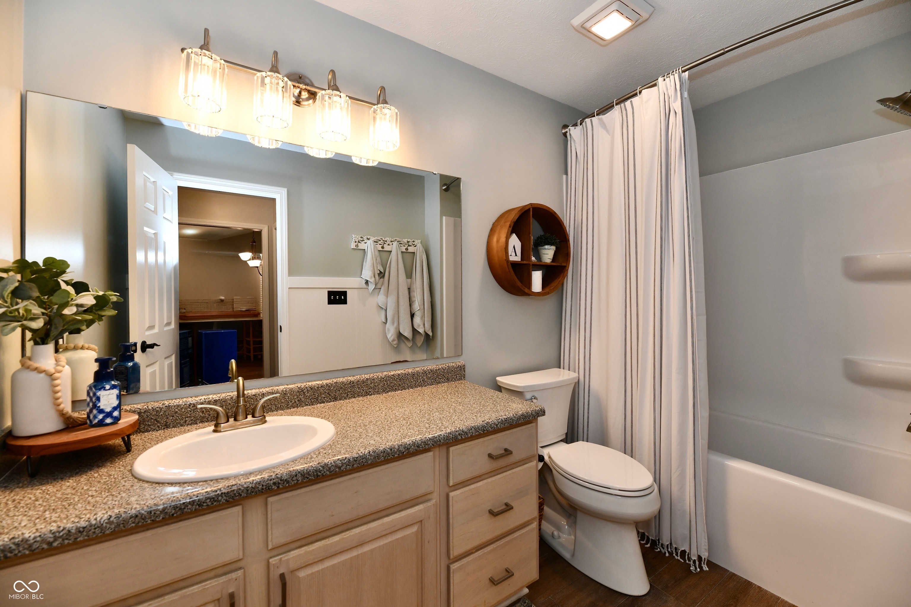 Bathroom with a granite vanity, large mirror, and bathtub behind a striped shower curtain.