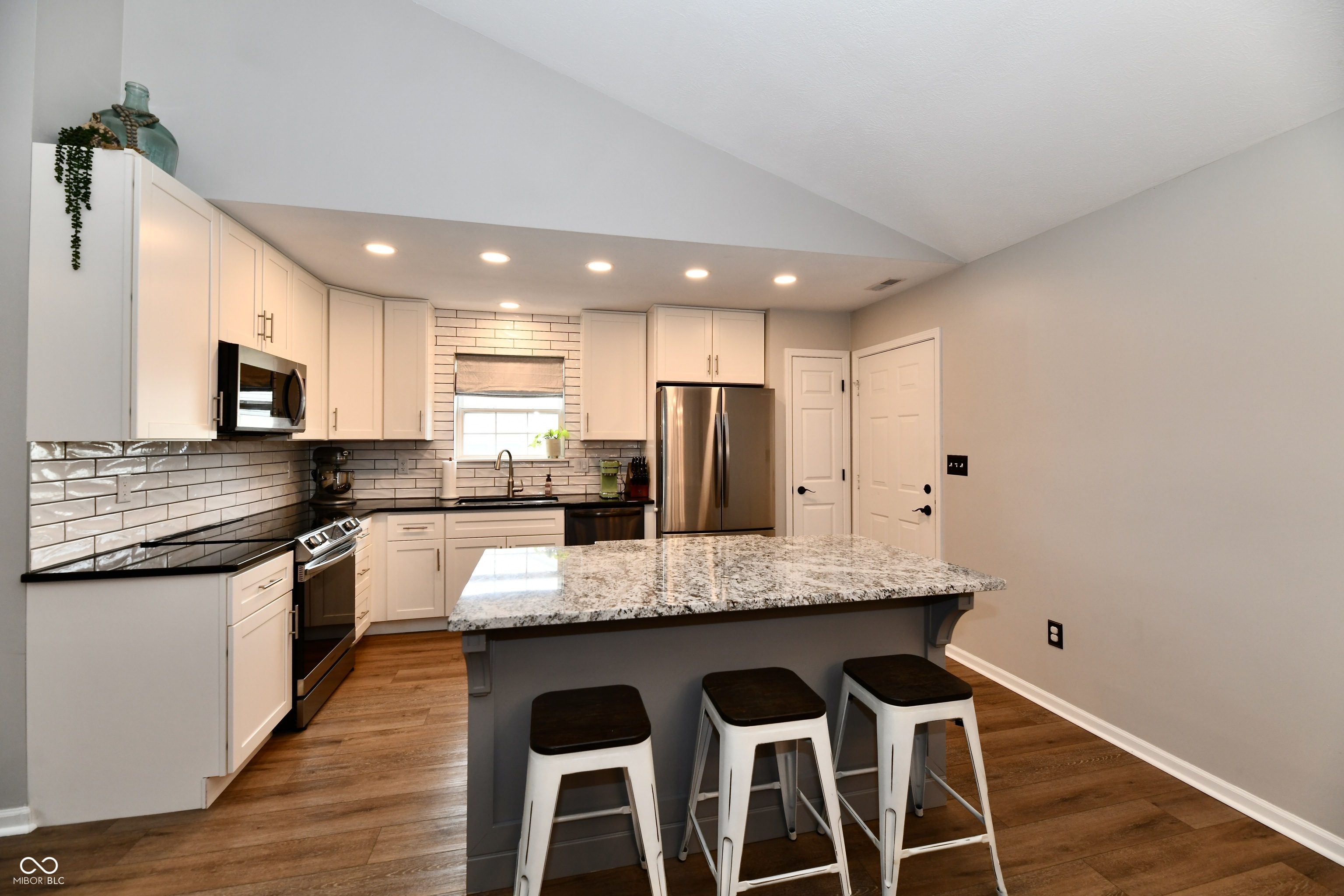 Kitchen with white cabinets, stainless appliances, and a granite island with three stools.