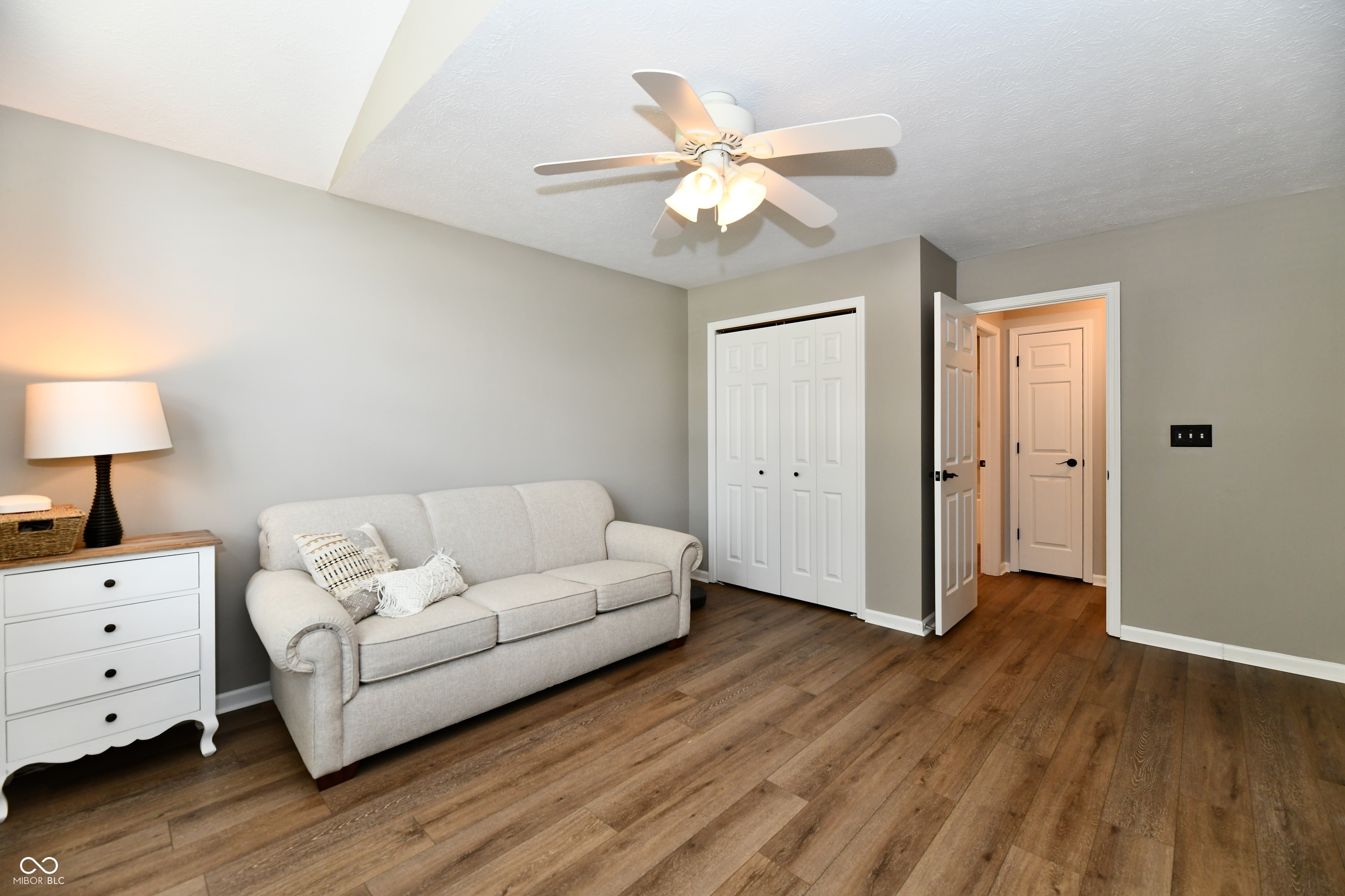 Living room with a light sofa, white closet doors, and brown wood-look flooring.