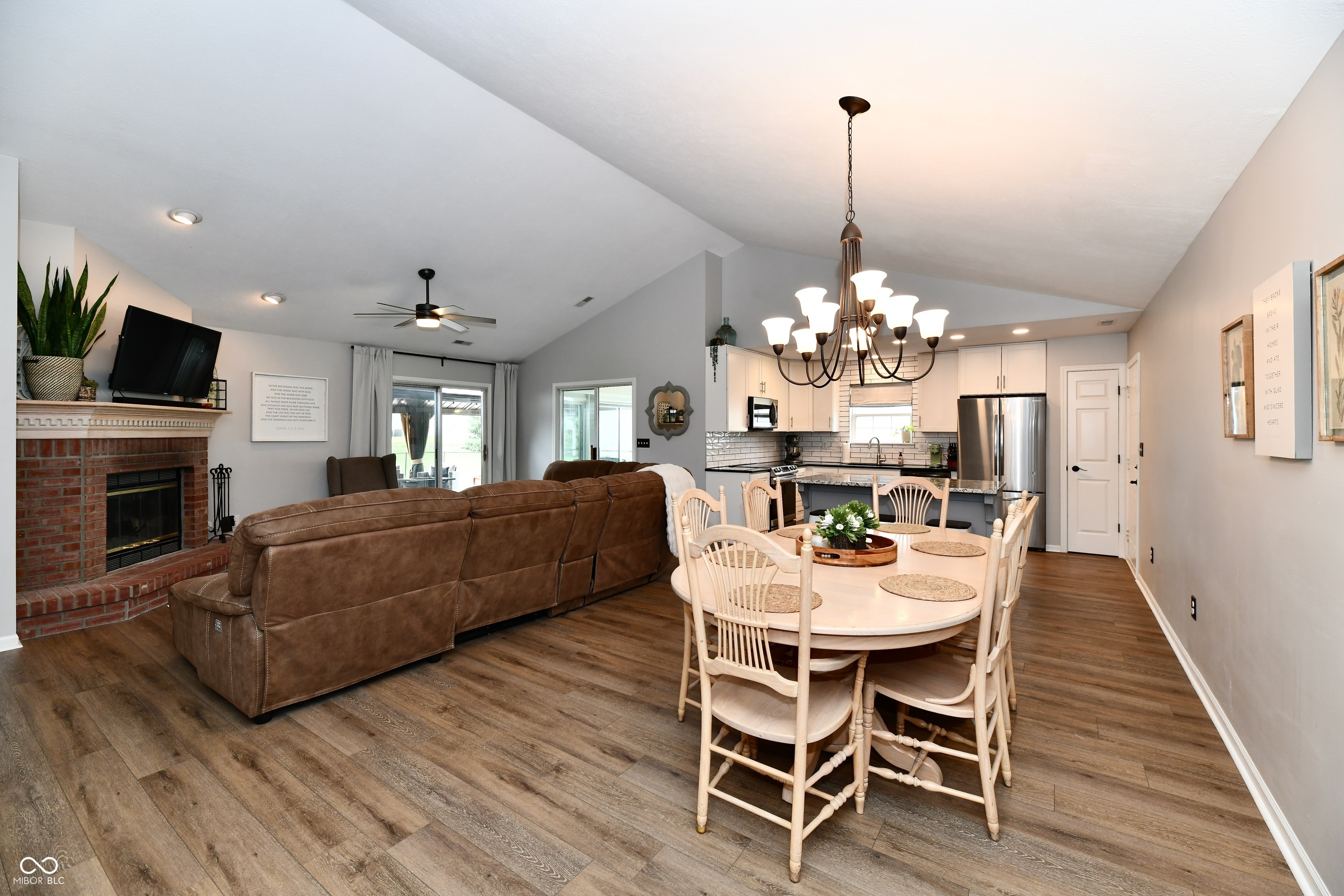 Open-plan living and dining area with a brick fireplace, brown sectional, and adjoining kitchen.