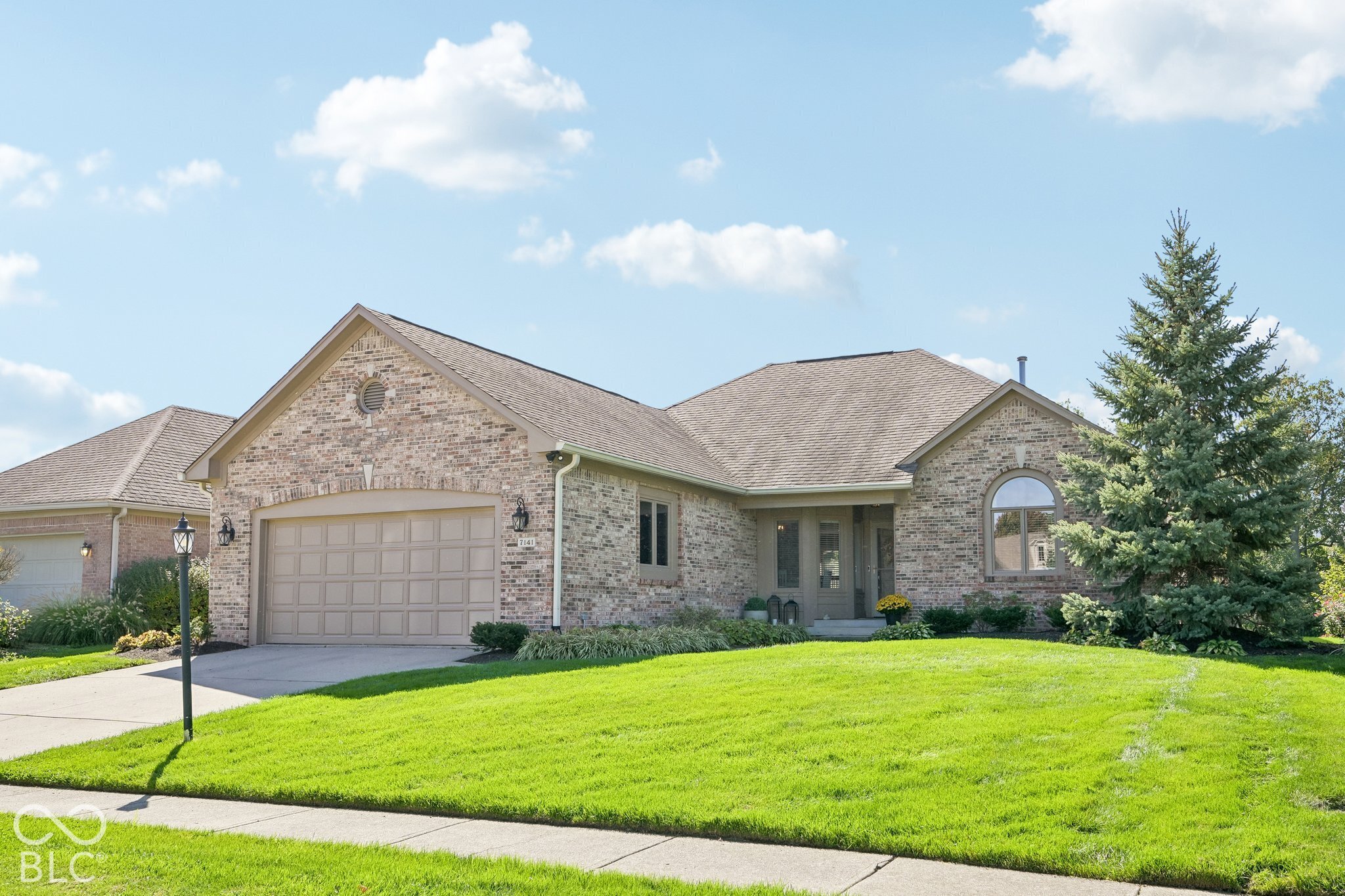 Brick home with a two-car garage, arched window, and landscaped front lawn.