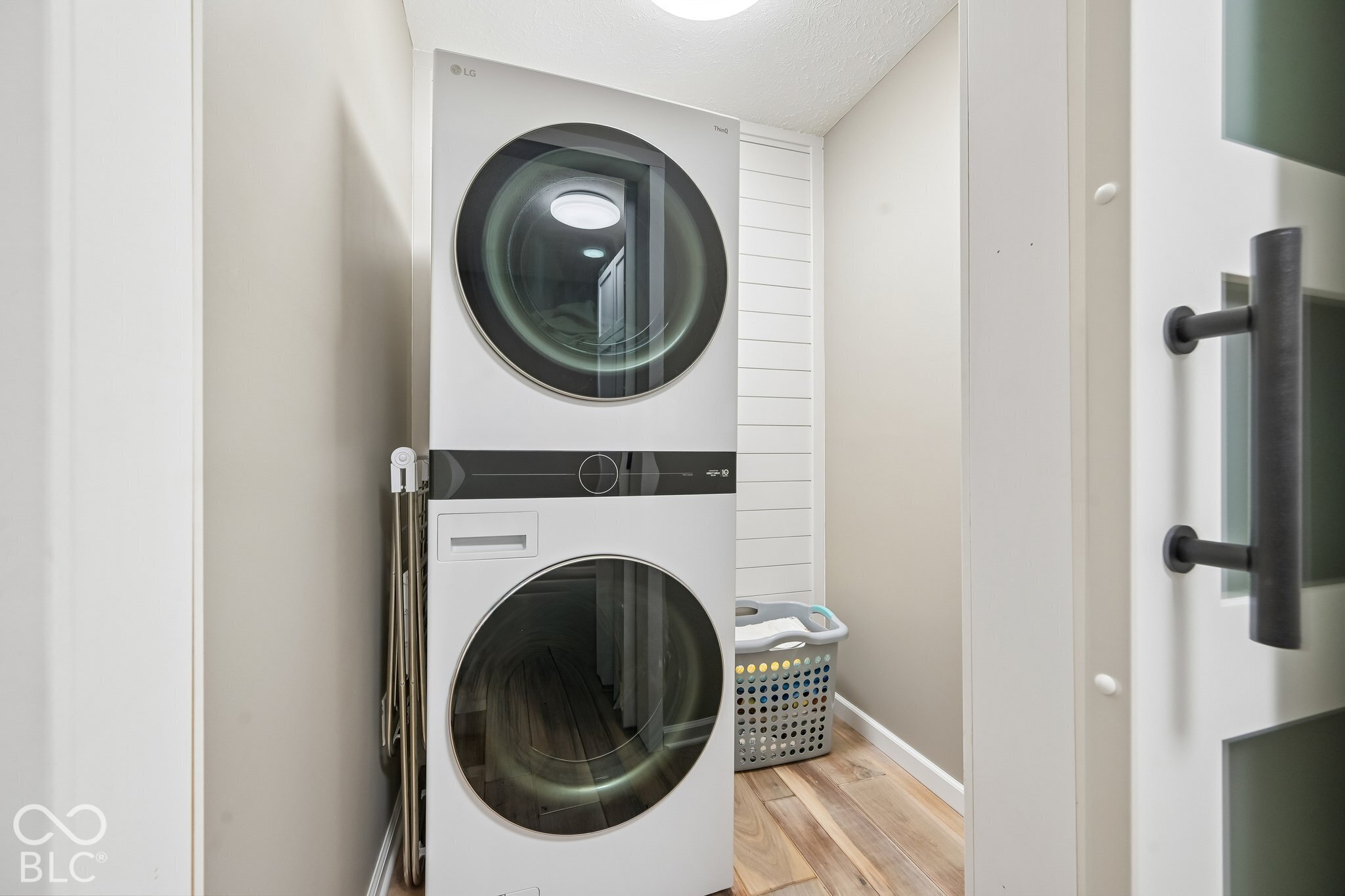 Laundry room with stacked washer and dryer, laundry basket, and wood-look flooring.