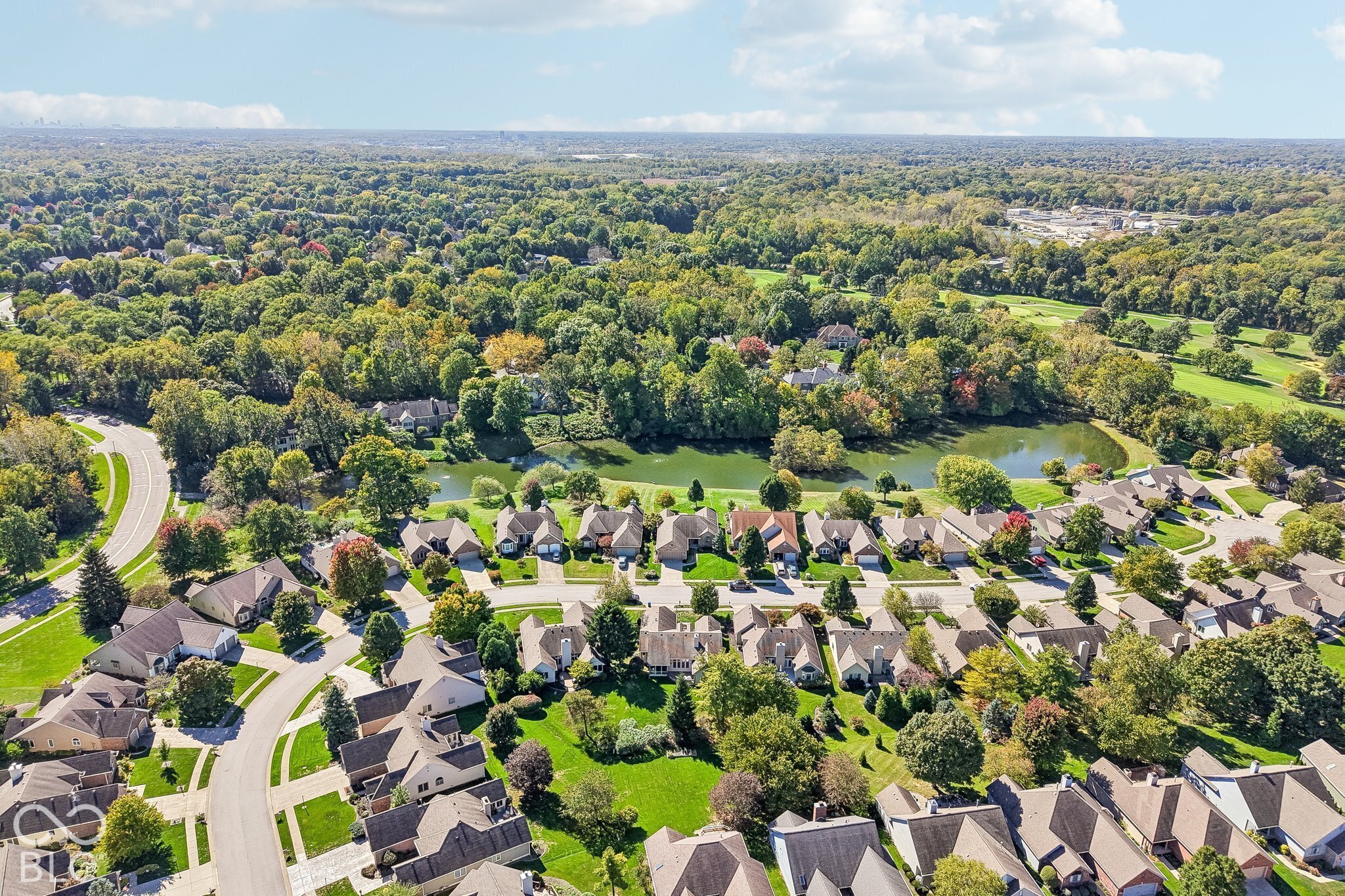 Aerial view of homes beside a pond, with a golf course and autumn trees beyond.