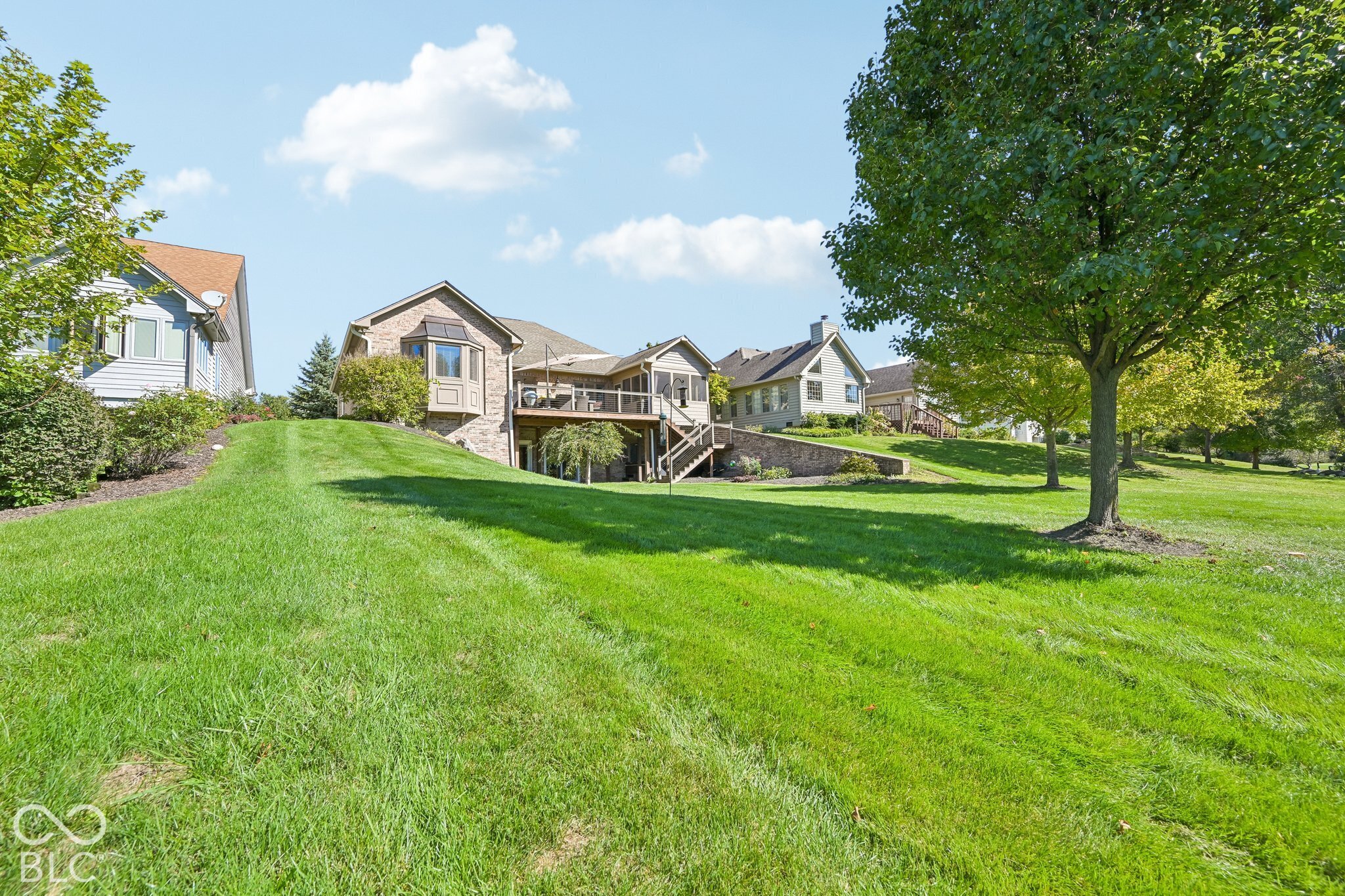 House with raised rear deck above a sloping lawn and mature shade trees.