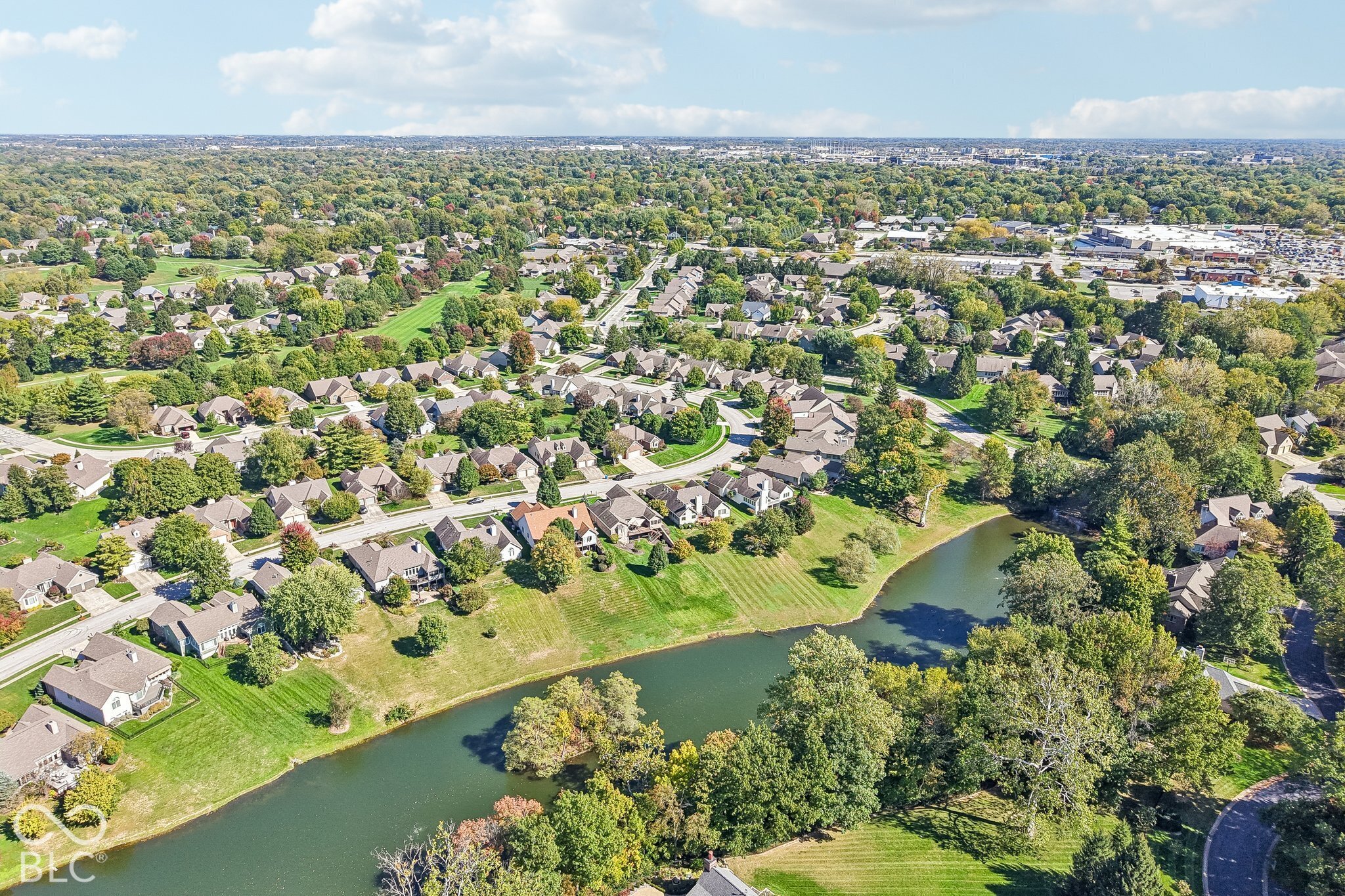 Aerial view of homes along a pond in a tree-lined neighborhood.
