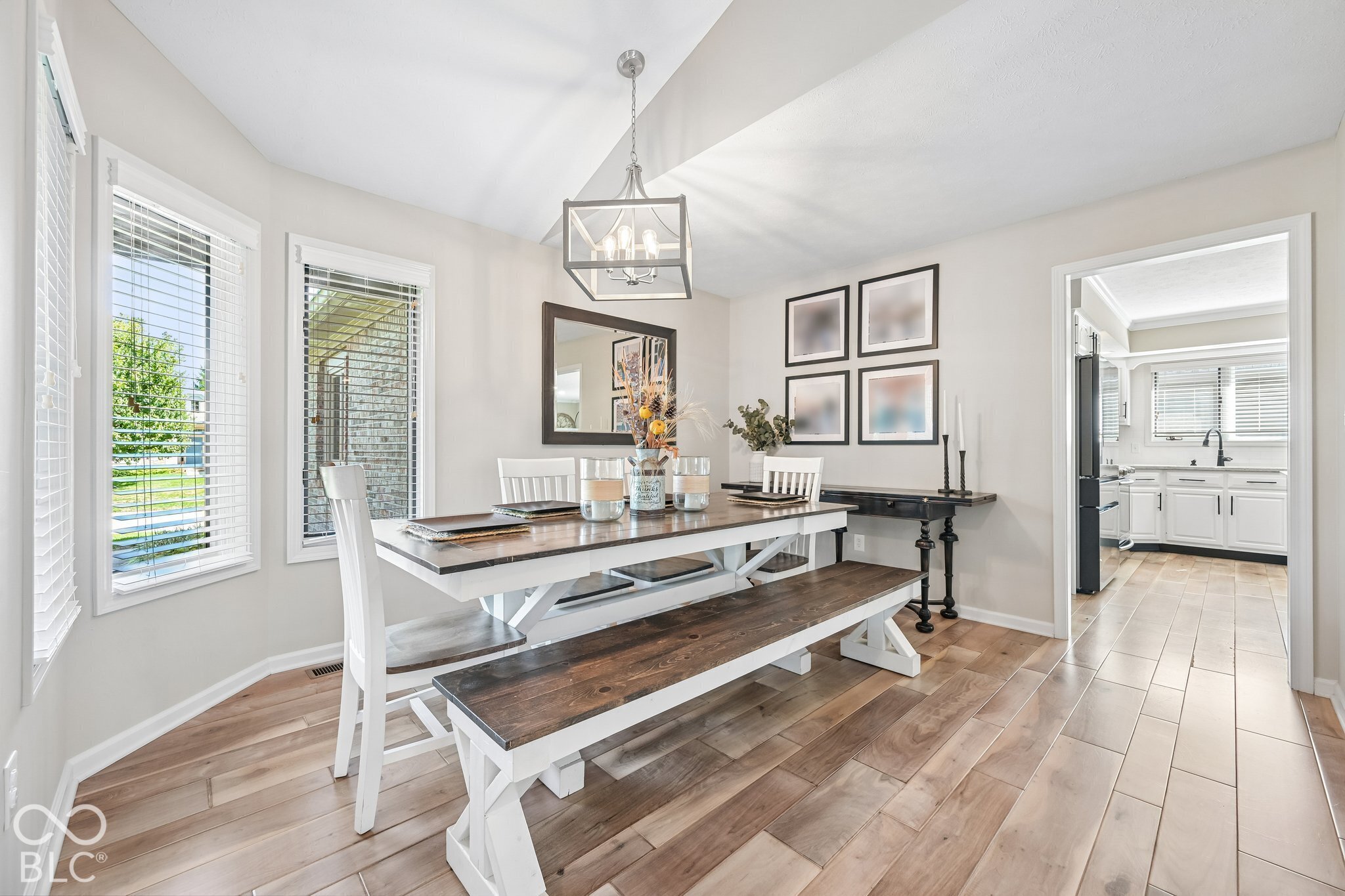 Dining room with a farmhouse table and benches, large windows, and a view into the kitchen.