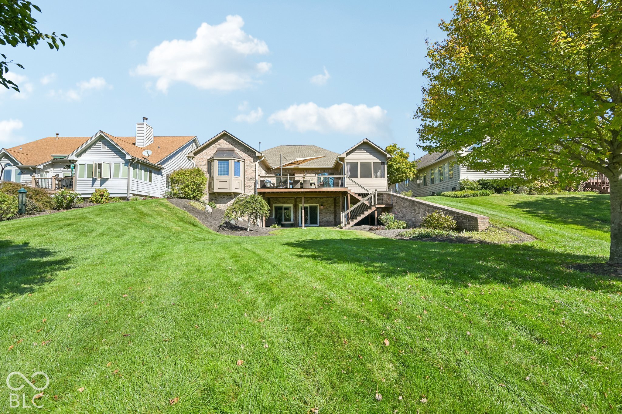 Home’s rear exterior with a raised deck, walkout lower level, and broad sloping lawn.