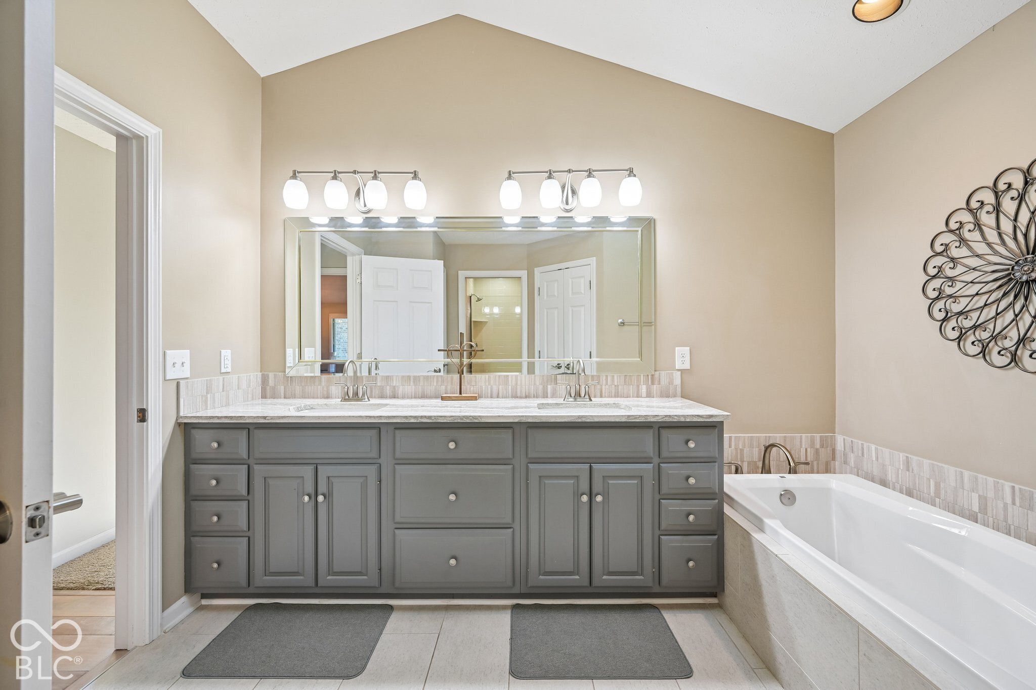 Bathroom with a gray double vanity, large mirror, and built-in soaking tub.