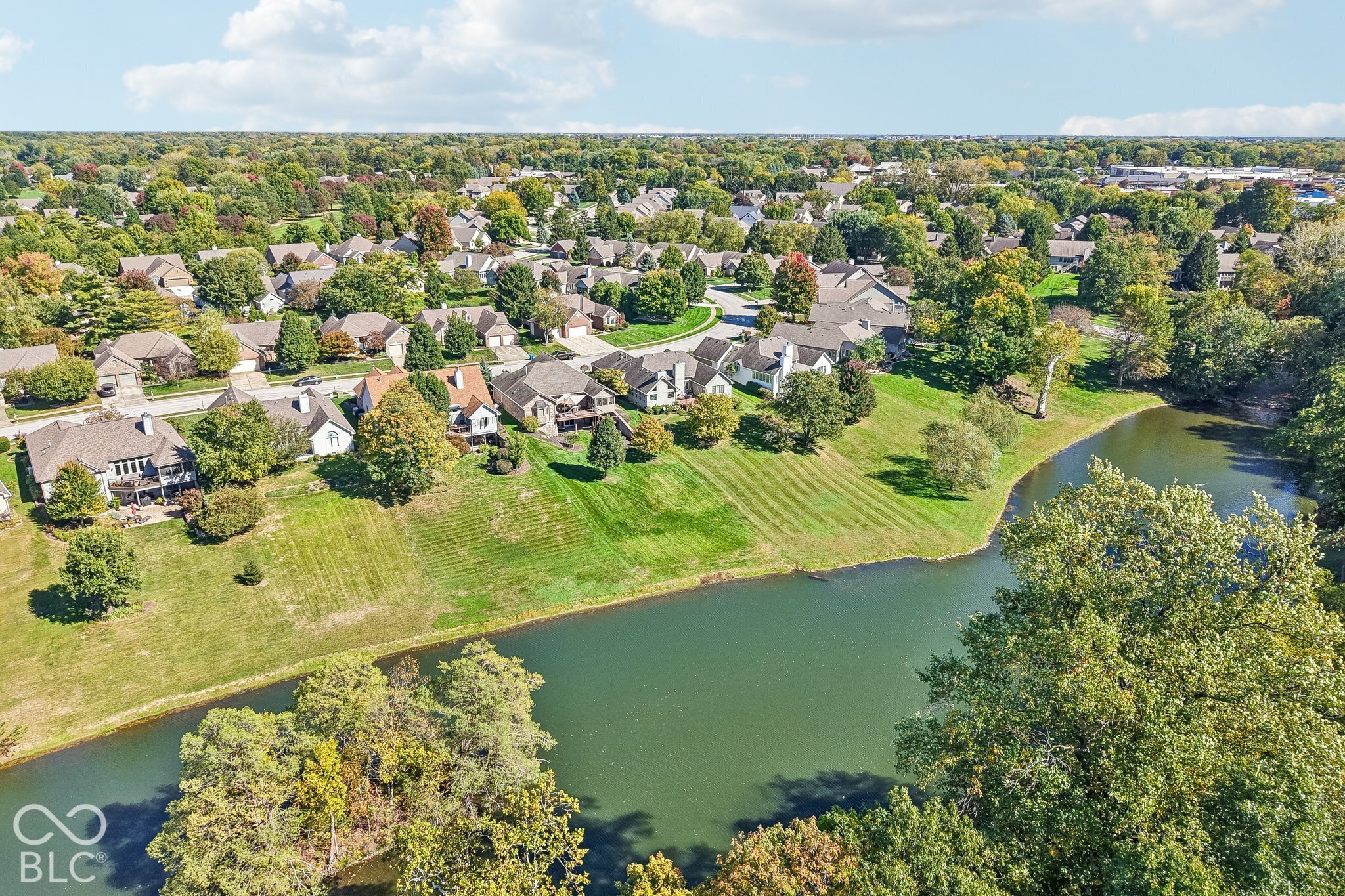 Aerial view of a lakeside neighborhood with homes, broad lawns, and mature trees.
