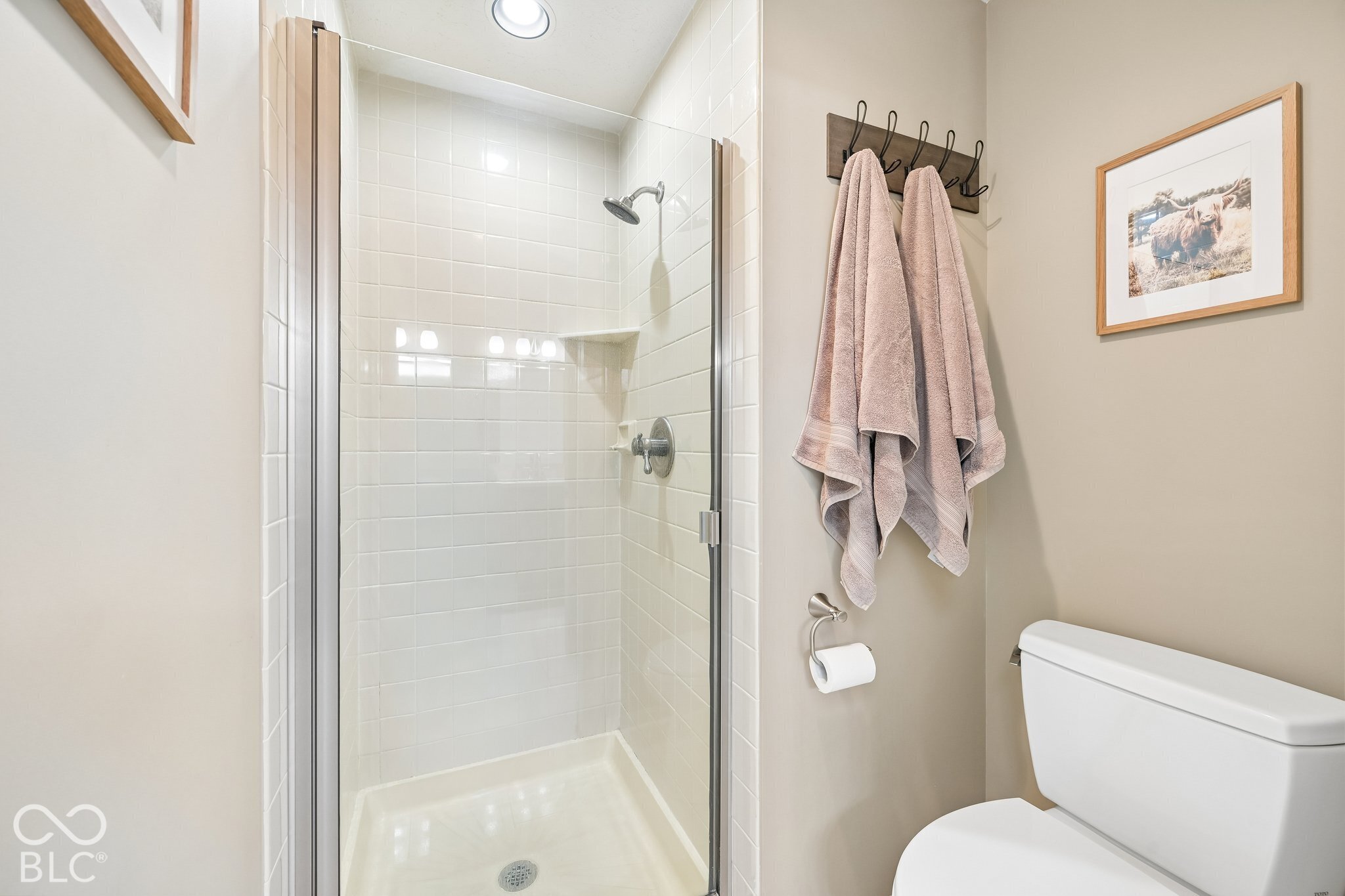 Bathroom with a glass-enclosed white-tiled shower, pink towels, and a toilet.