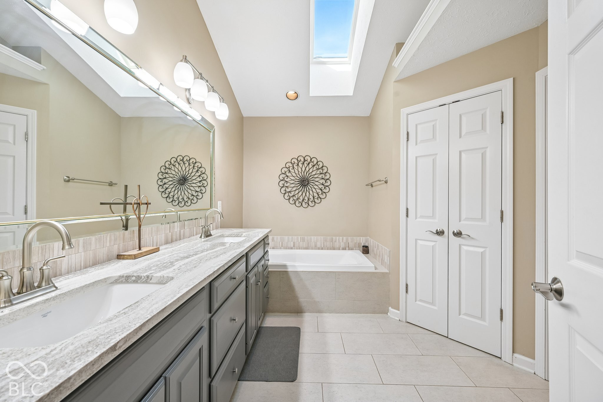 Bathroom with a long double-sink vanity, bathtub, and skylight.