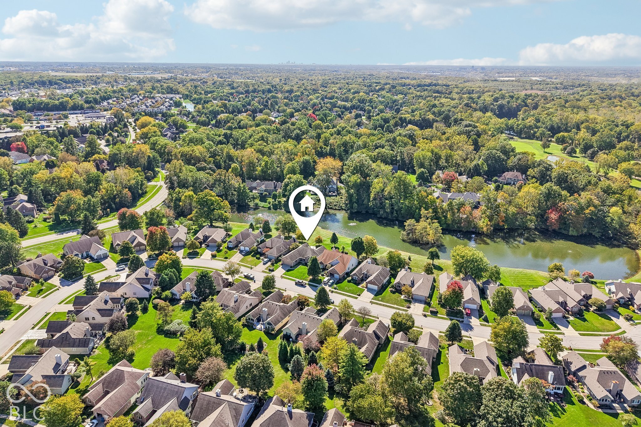 Aerial neighborhood view with a marked home beside a tree-lined river.