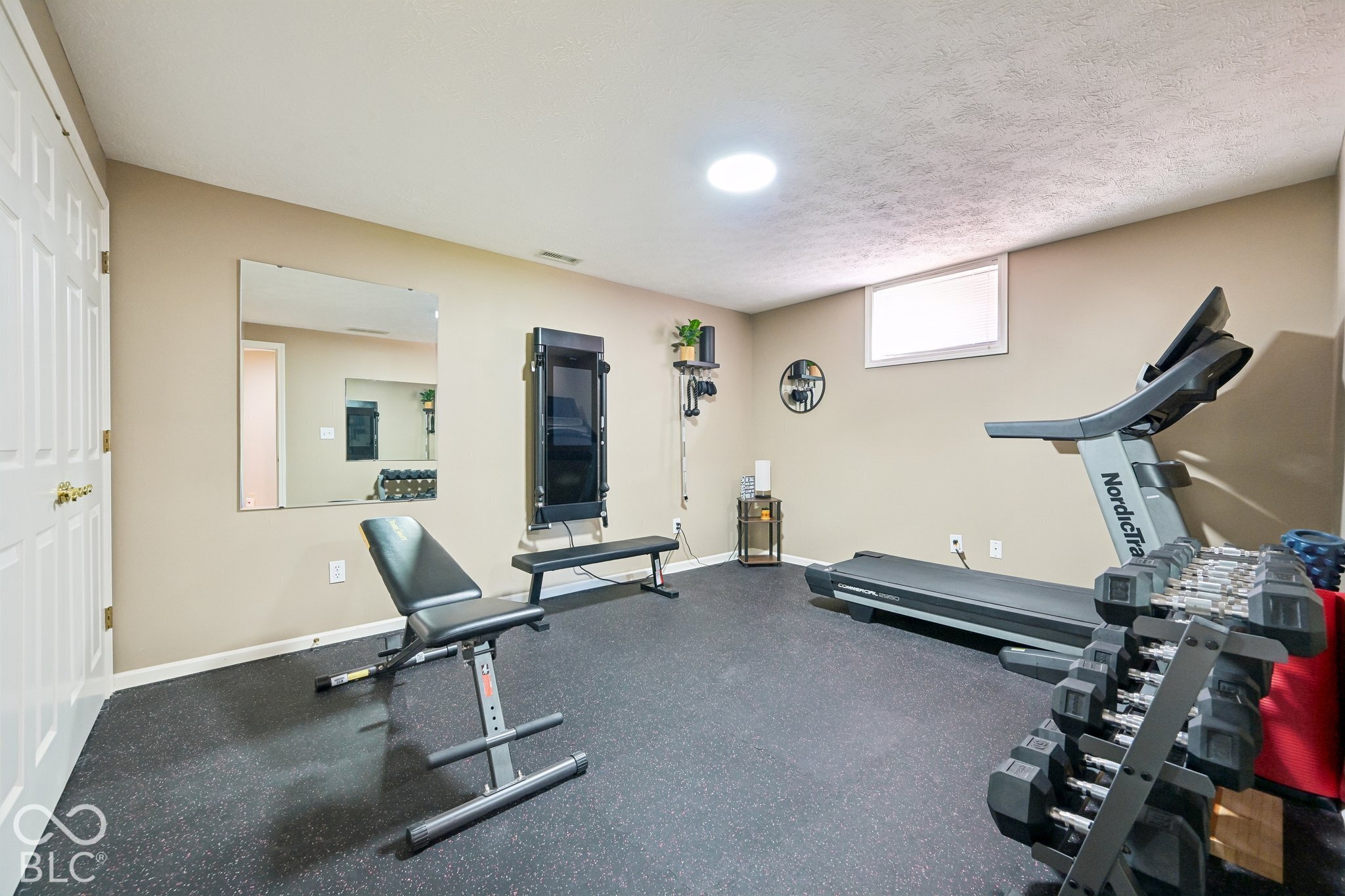 Home gym with a wall mirror, treadmill, weight bench, and dumbbell rack.