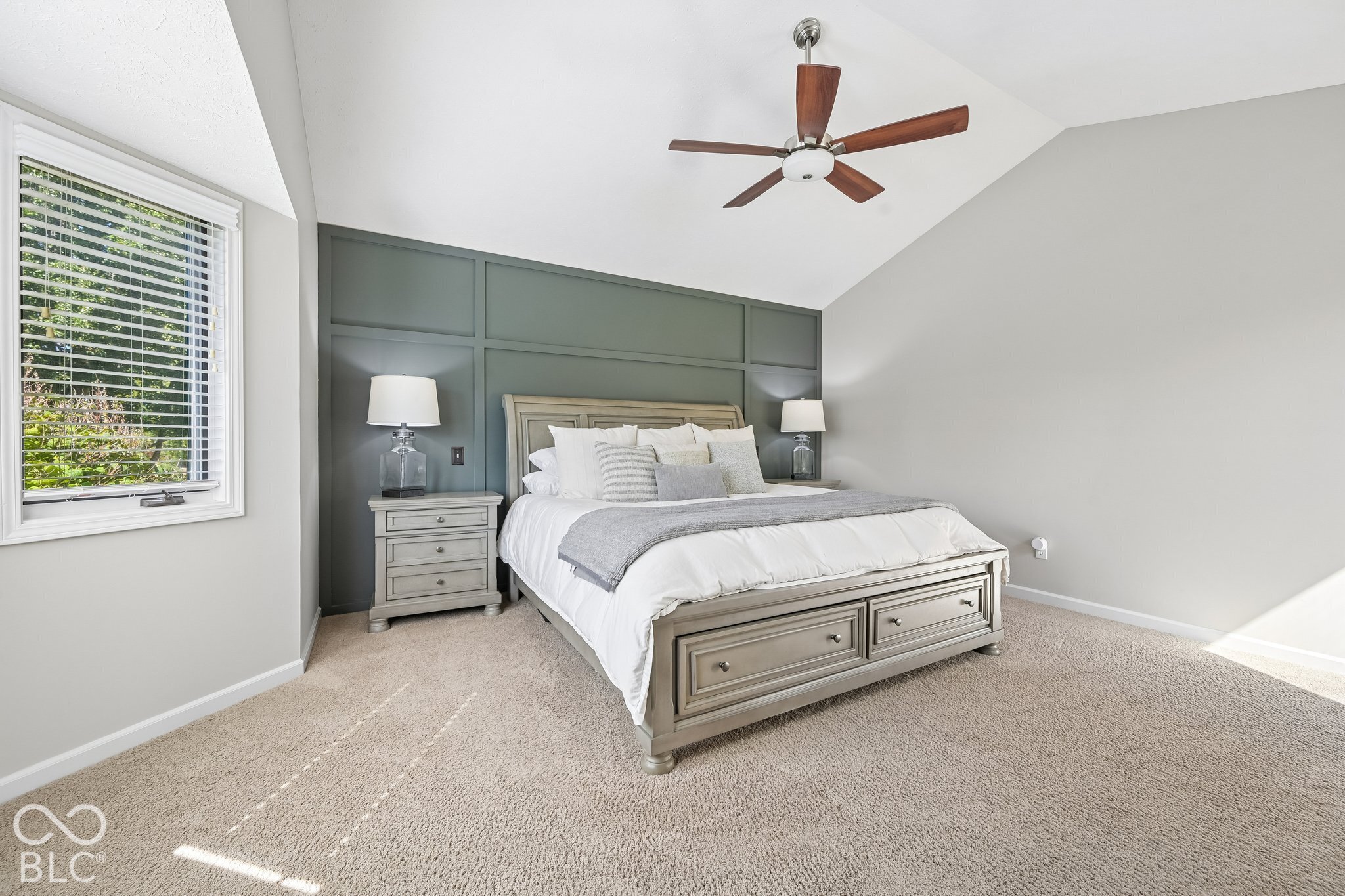 Staged bedroom with a large bed, gray paneled accent wall, and daylight through a window.