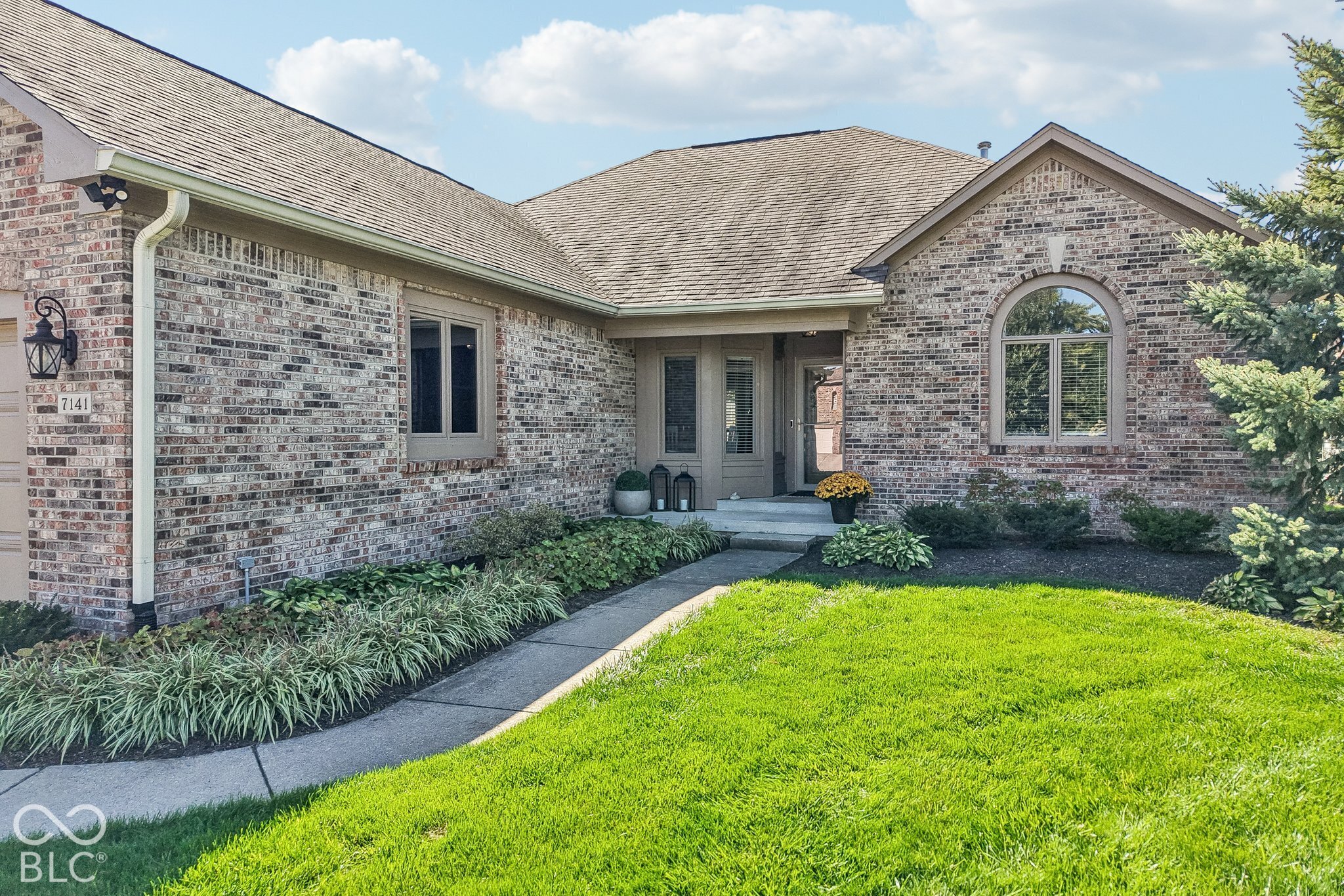 Brick home with an arched front window, landscaped entry, and bright green lawn.