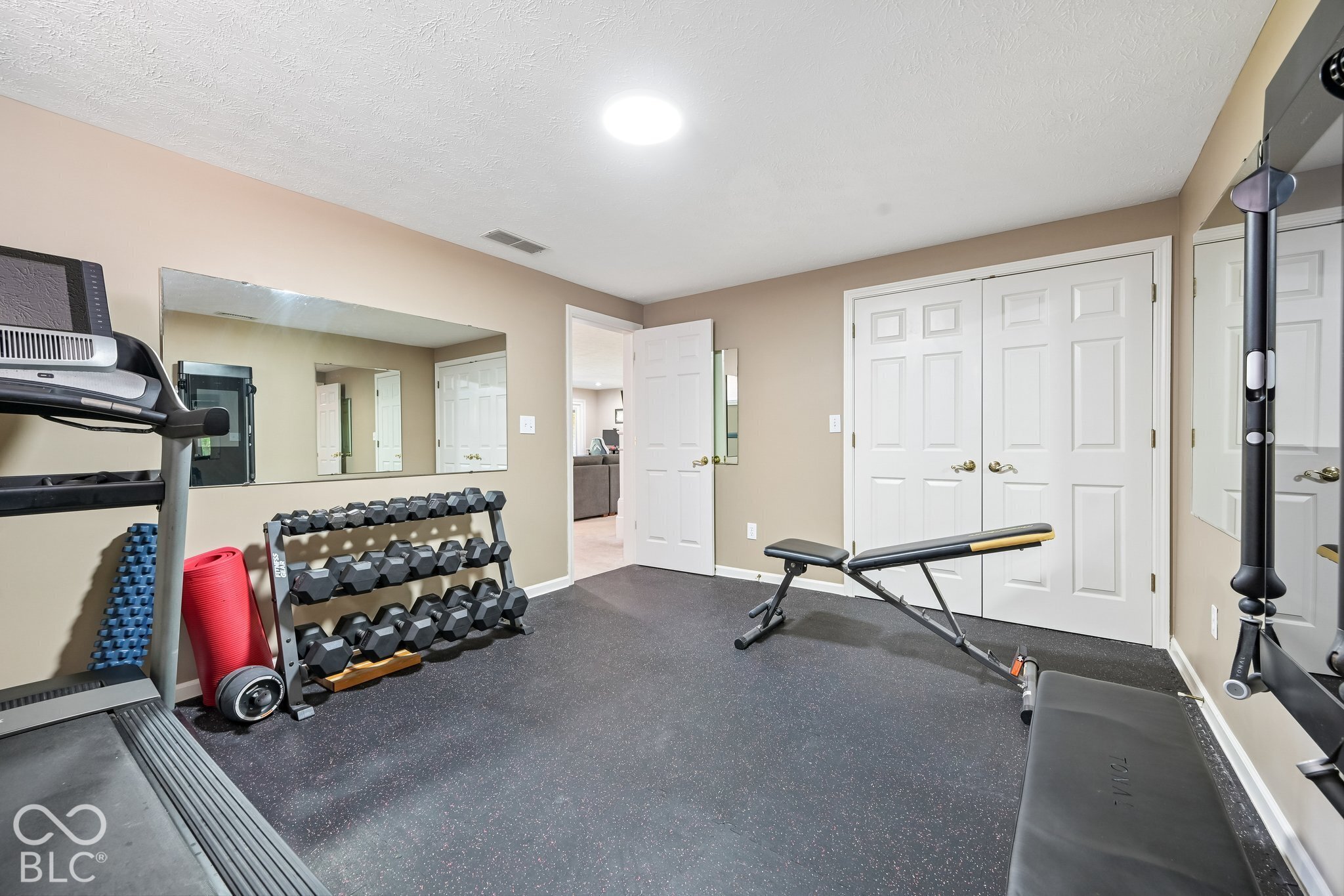 Home gym with a mirrored wall, dumbbell rack, treadmill, and weight bench.