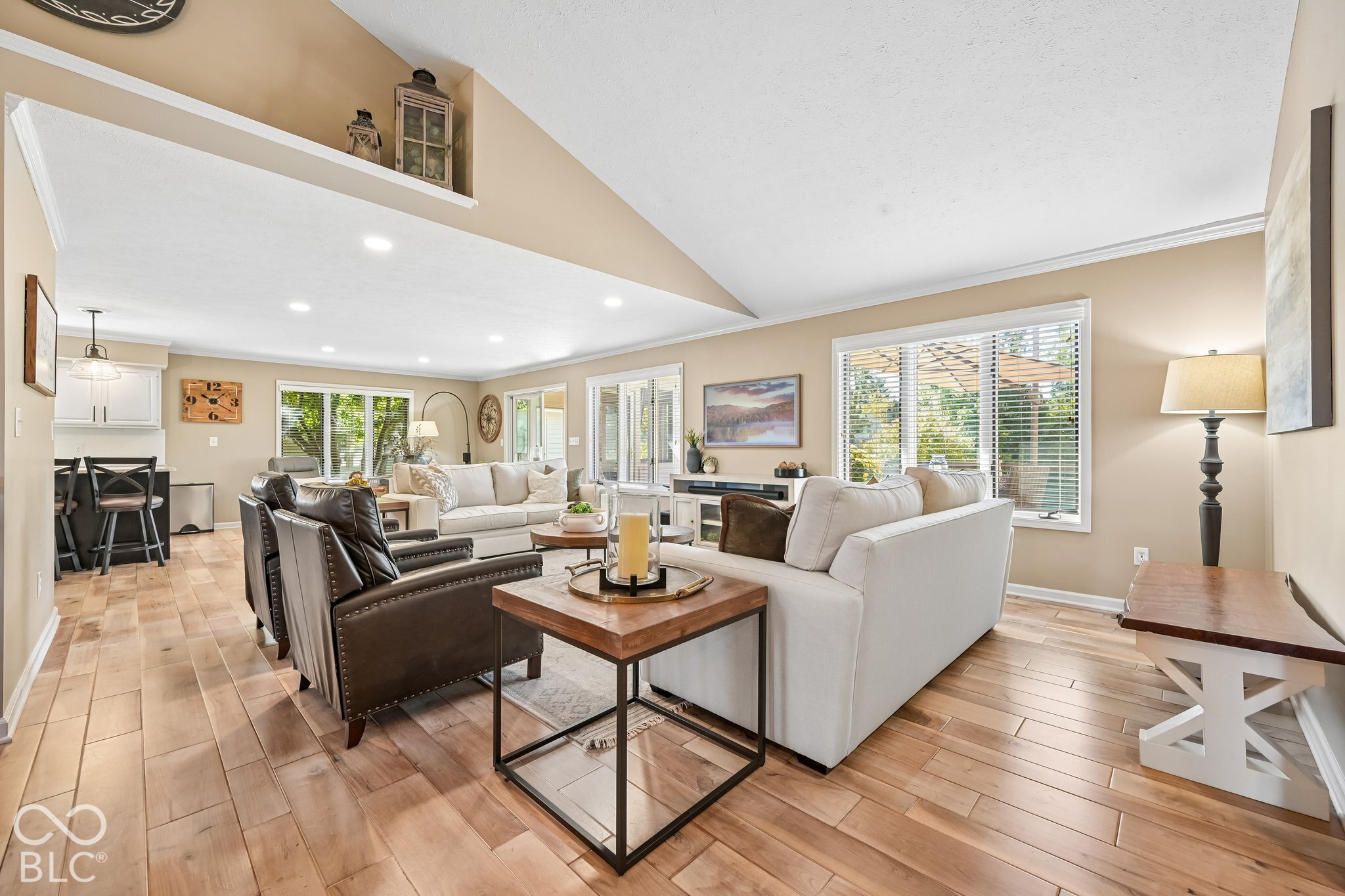 Open-plan living room with vaulted ceiling, white sofas, dark leather chairs, and wood-look tile flooring.