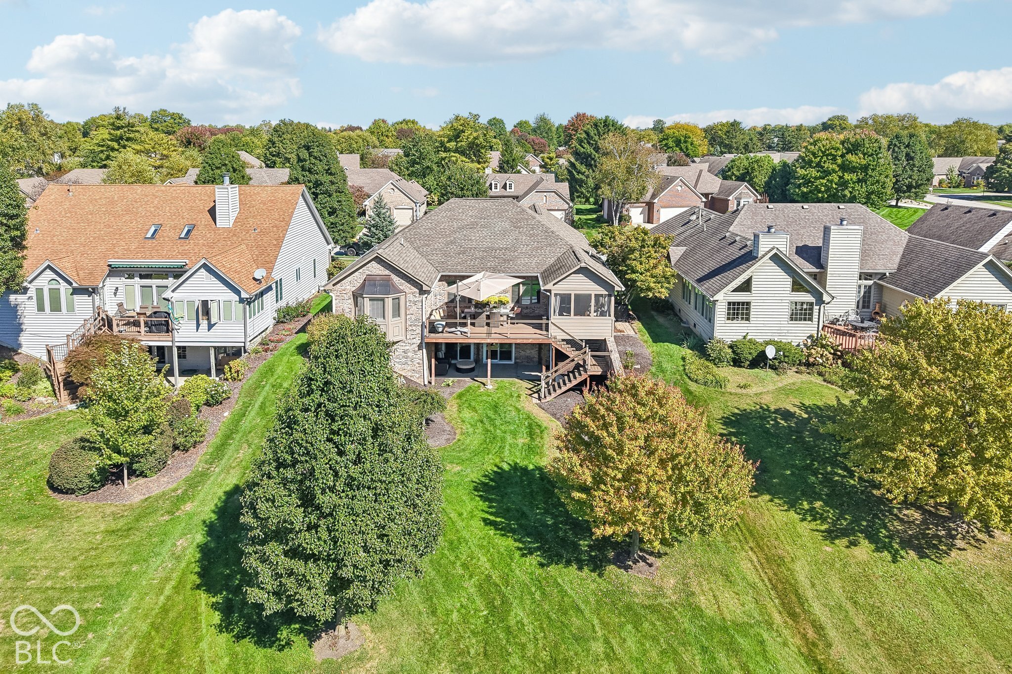 Aerial view of a home’s rear deck and landscaped yard among neighboring houses.