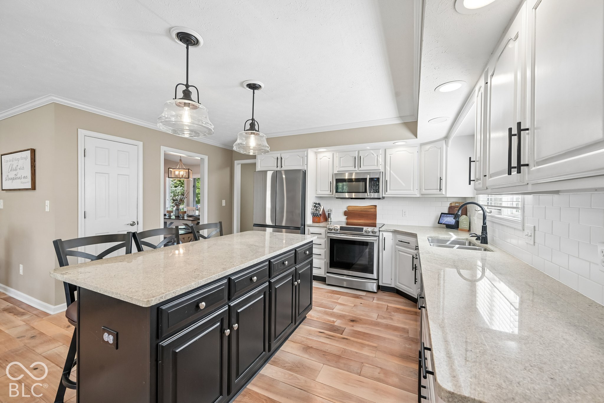 Kitchen with a dark island, light stone counters, white cabinets, and stainless steel appliances.