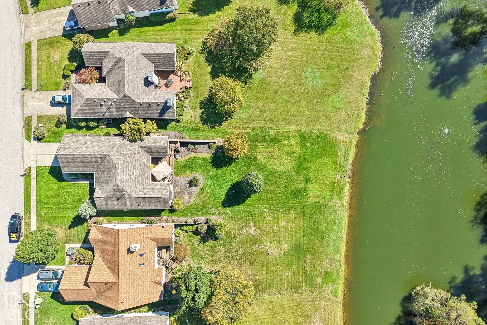 Aerial view of homes beside a pond, with spacious lawns and landscaped yards.
