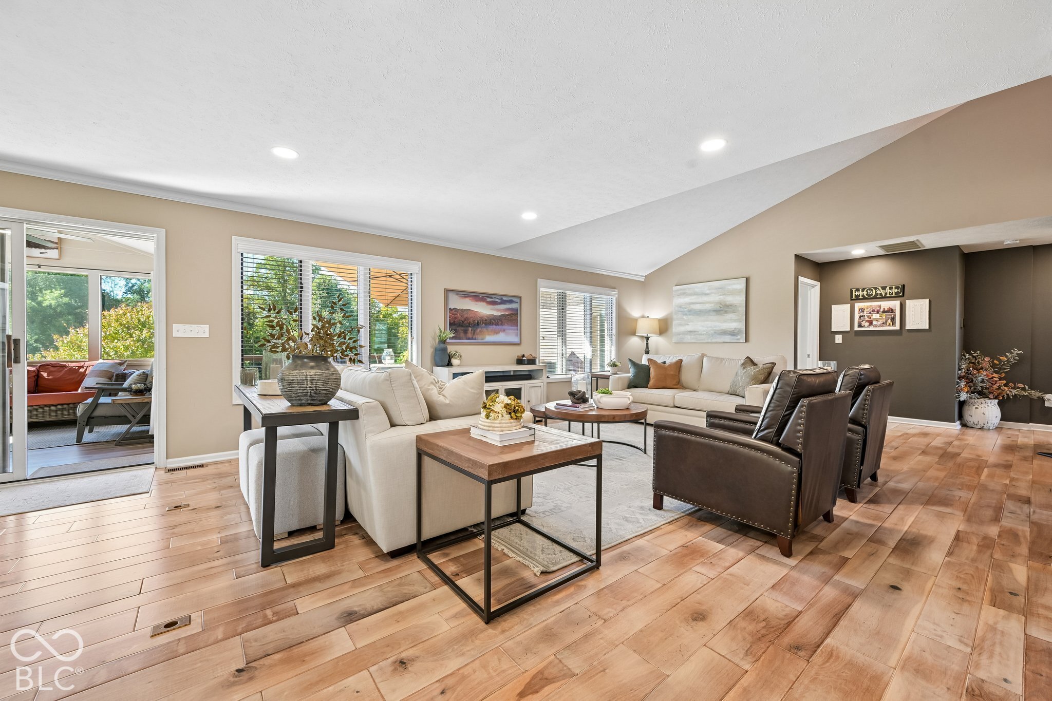 Furnished living room with cream sofas, dark leather armchairs, and wide-plank wood floors.