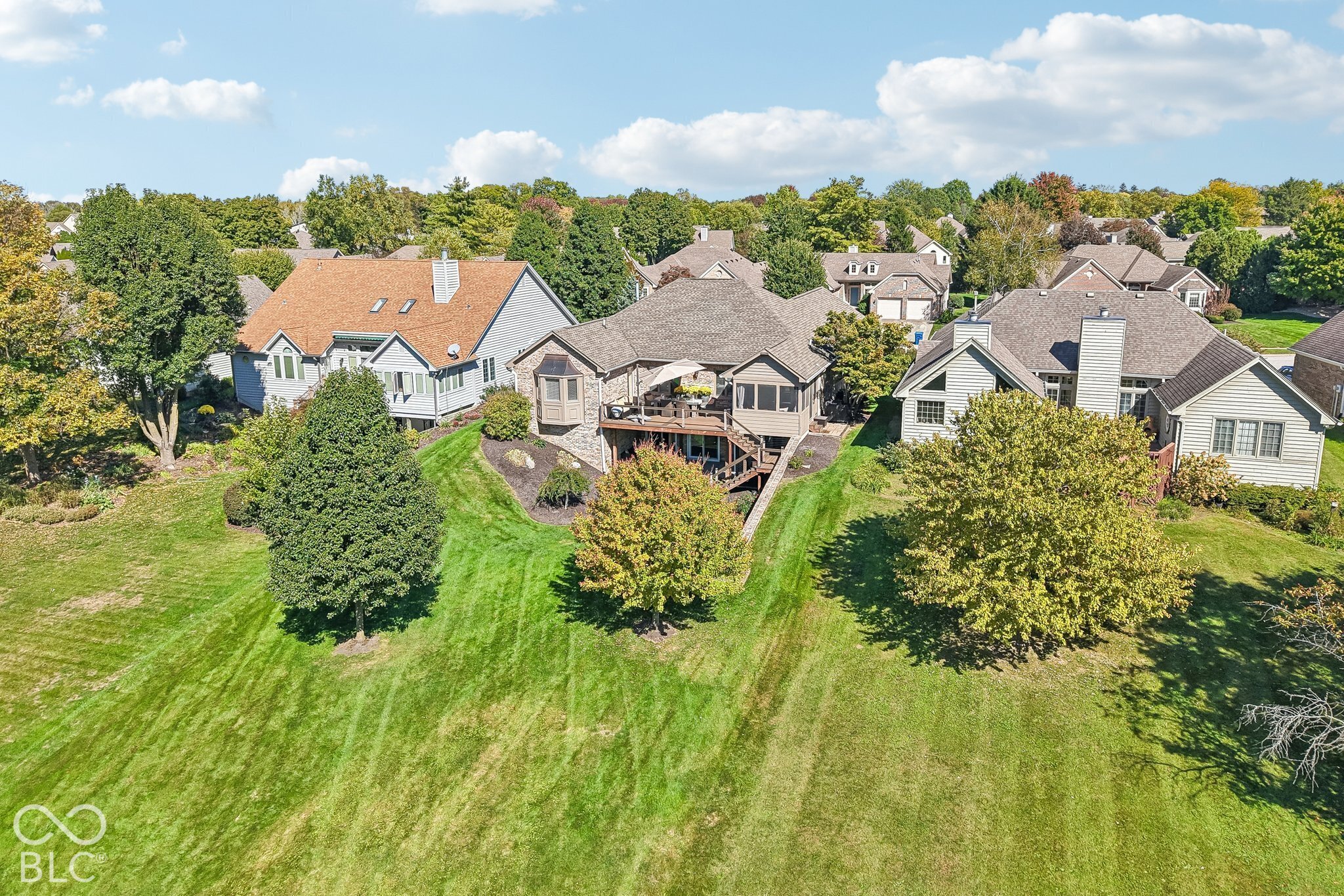 Aerial view of a home with a raised deck and spacious landscaped lawn.
