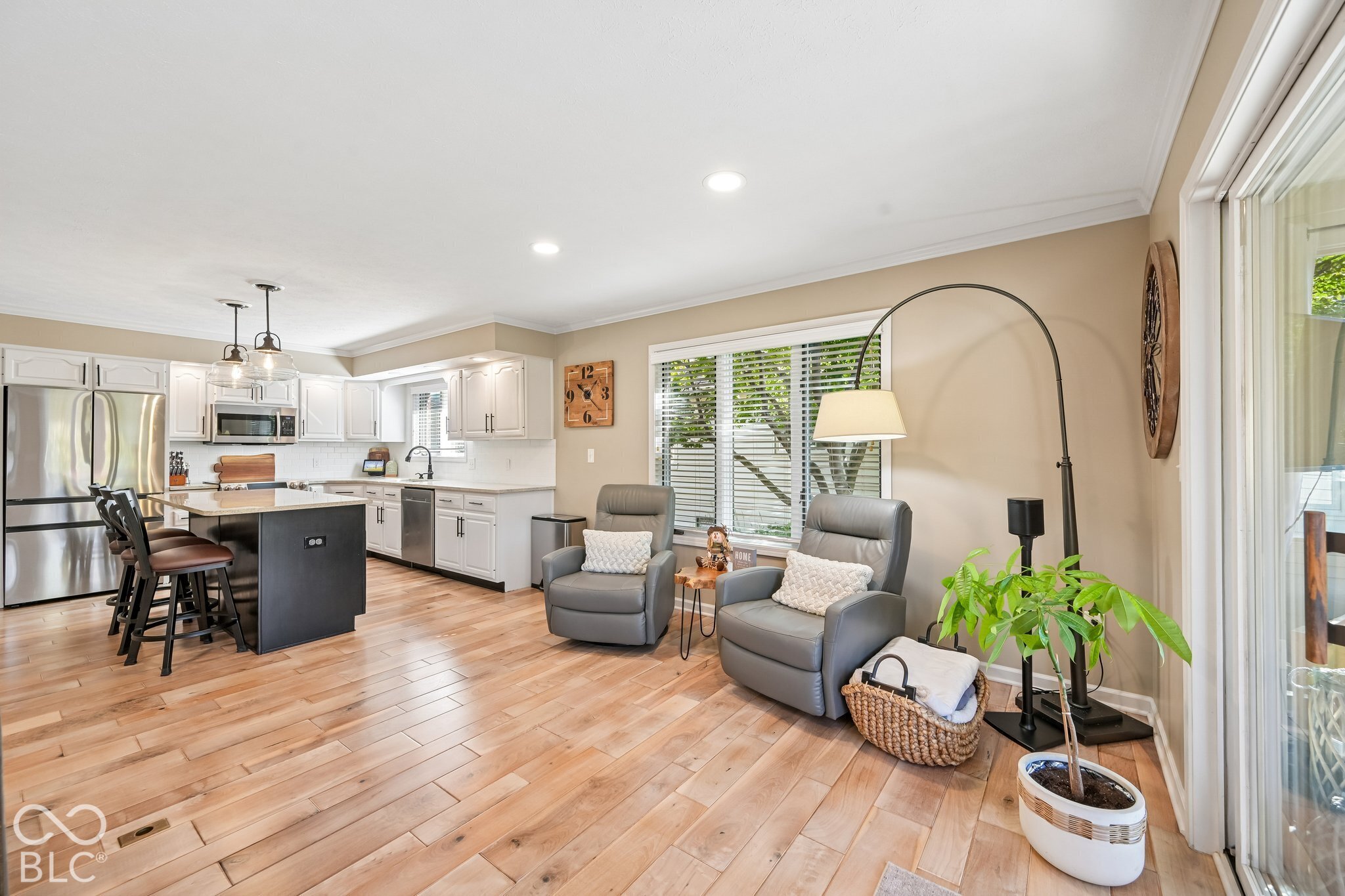 Open kitchen and living area with a dark island, gray recliners, and light wood floors.