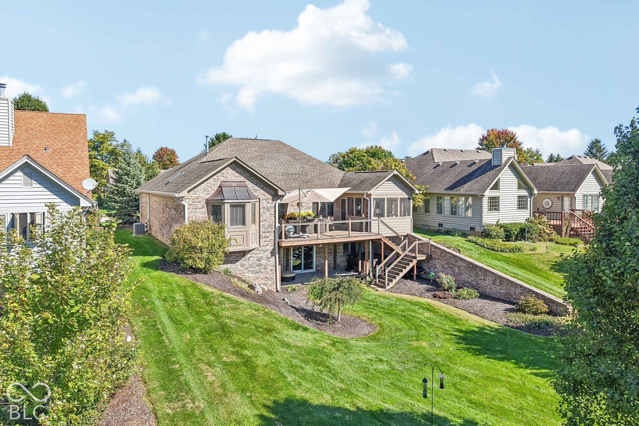 Rear of a brick home with a raised deck, outdoor seating, and a broad green lawn.