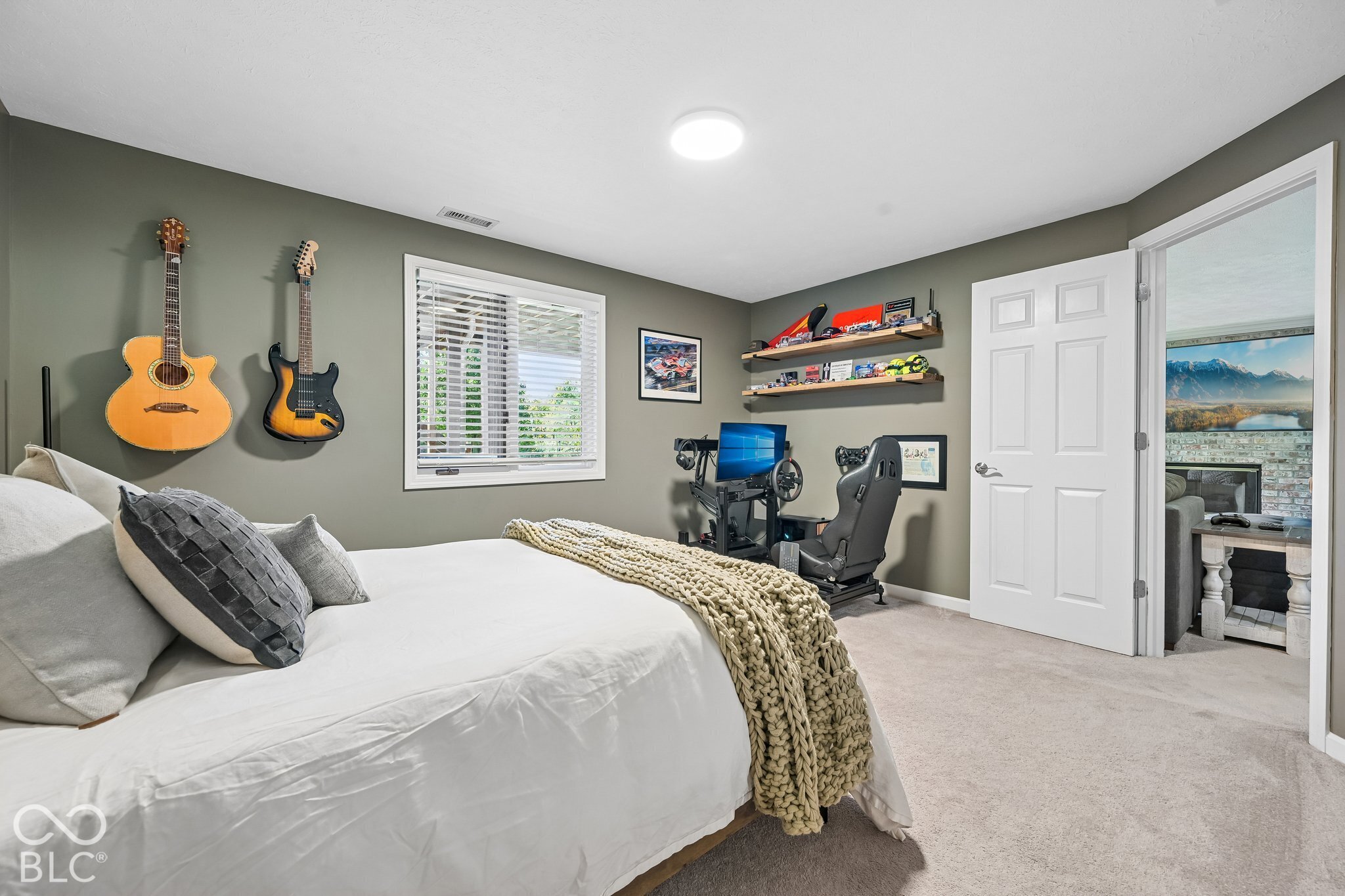 Bedroom with wall-mounted guitars, a racing simulator, and a chunky knit blanket on the bed.