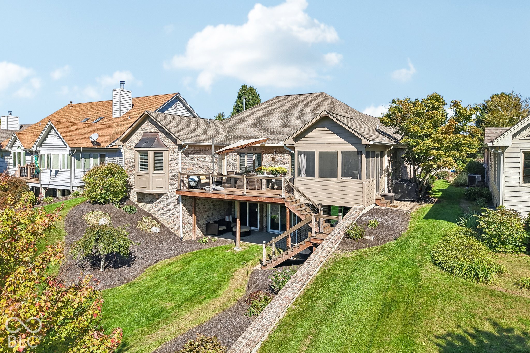 Home’s rear exterior with a raised deck, screened porch, and landscaped lawn.