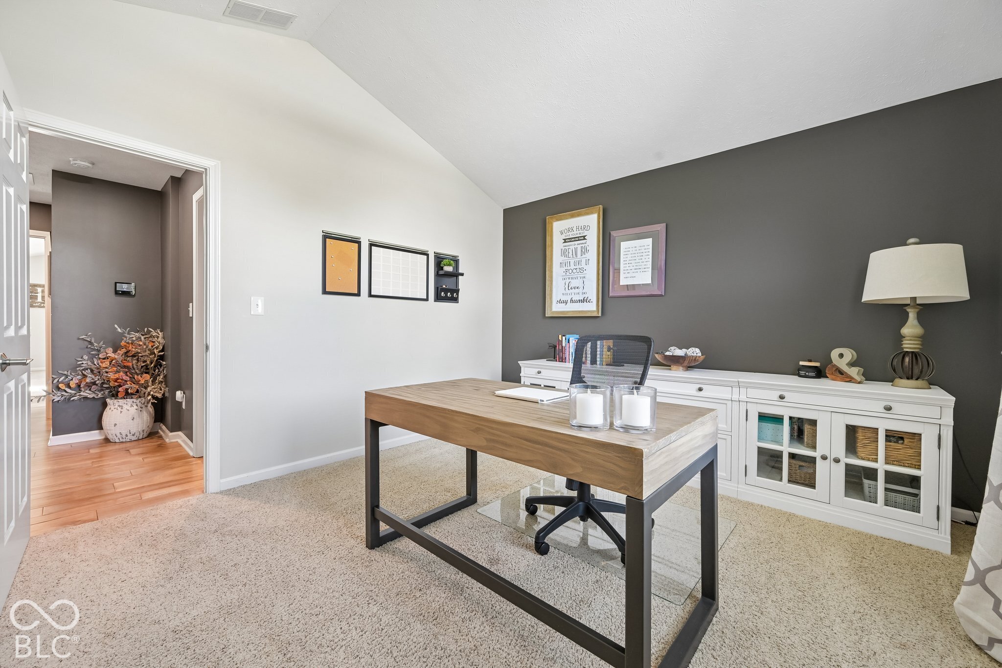 Furnished home office with a wood desk, black chair, and white credenza against a gray accent wall.