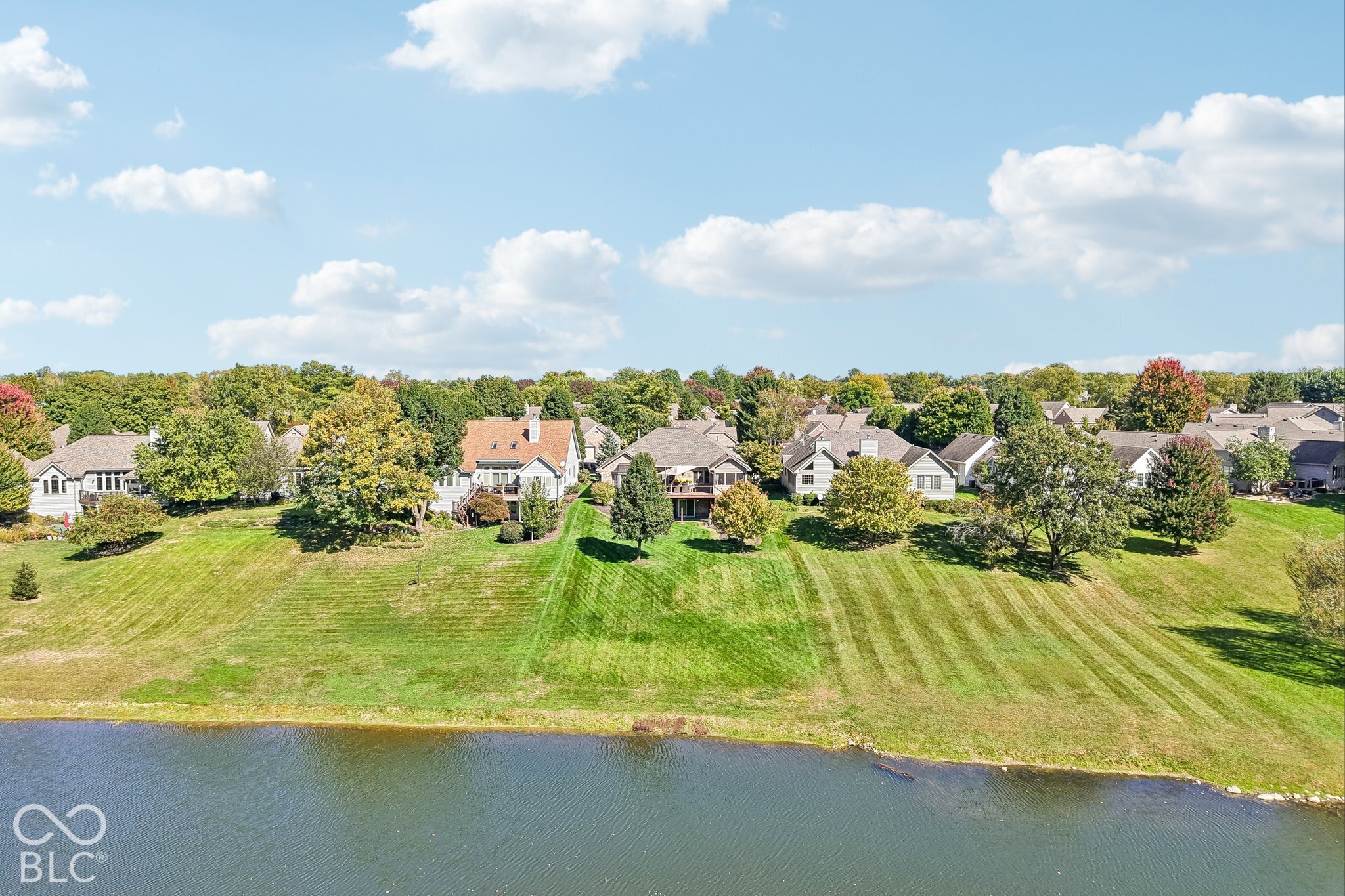 Aerial view of homes beside a pond, with broad lawns and mature trees.