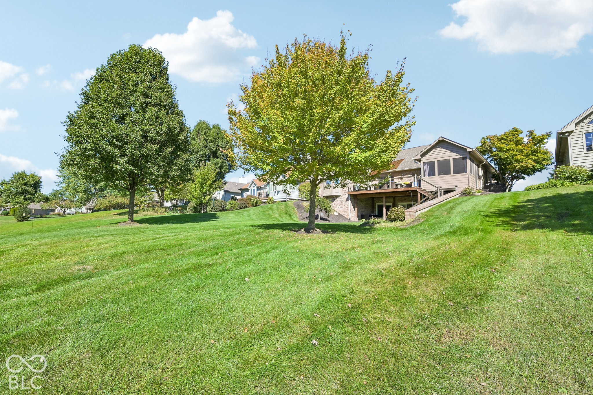 House behind a broad sloping lawn, with mature trees, a raised deck, and a screened porch.