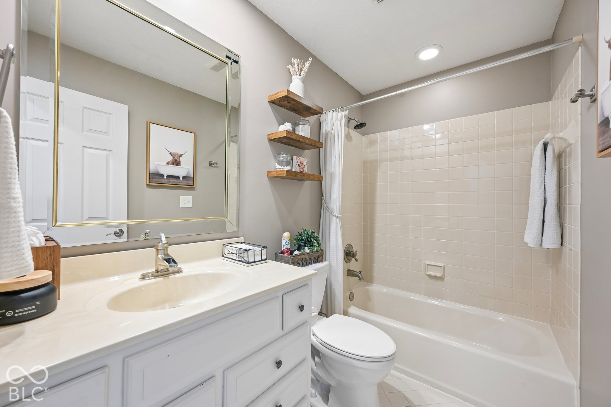 Bathroom with a white vanity, gold-trimmed mirror, and tiled bathtub surround.