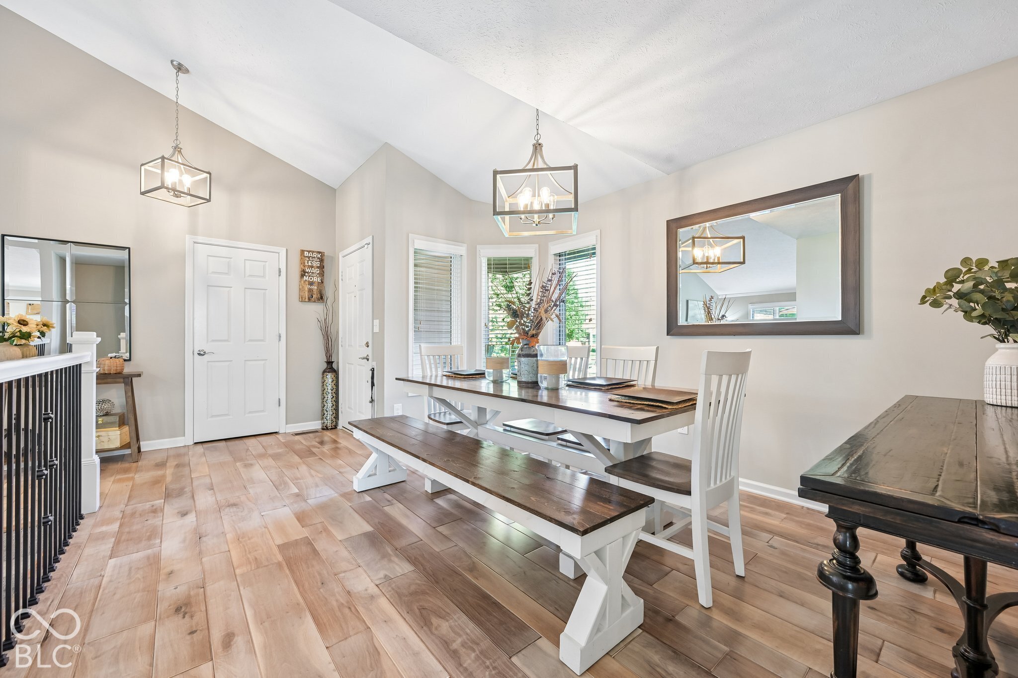 Dining room with vaulted ceiling, wood floors, and a long table with white chairs and bench.