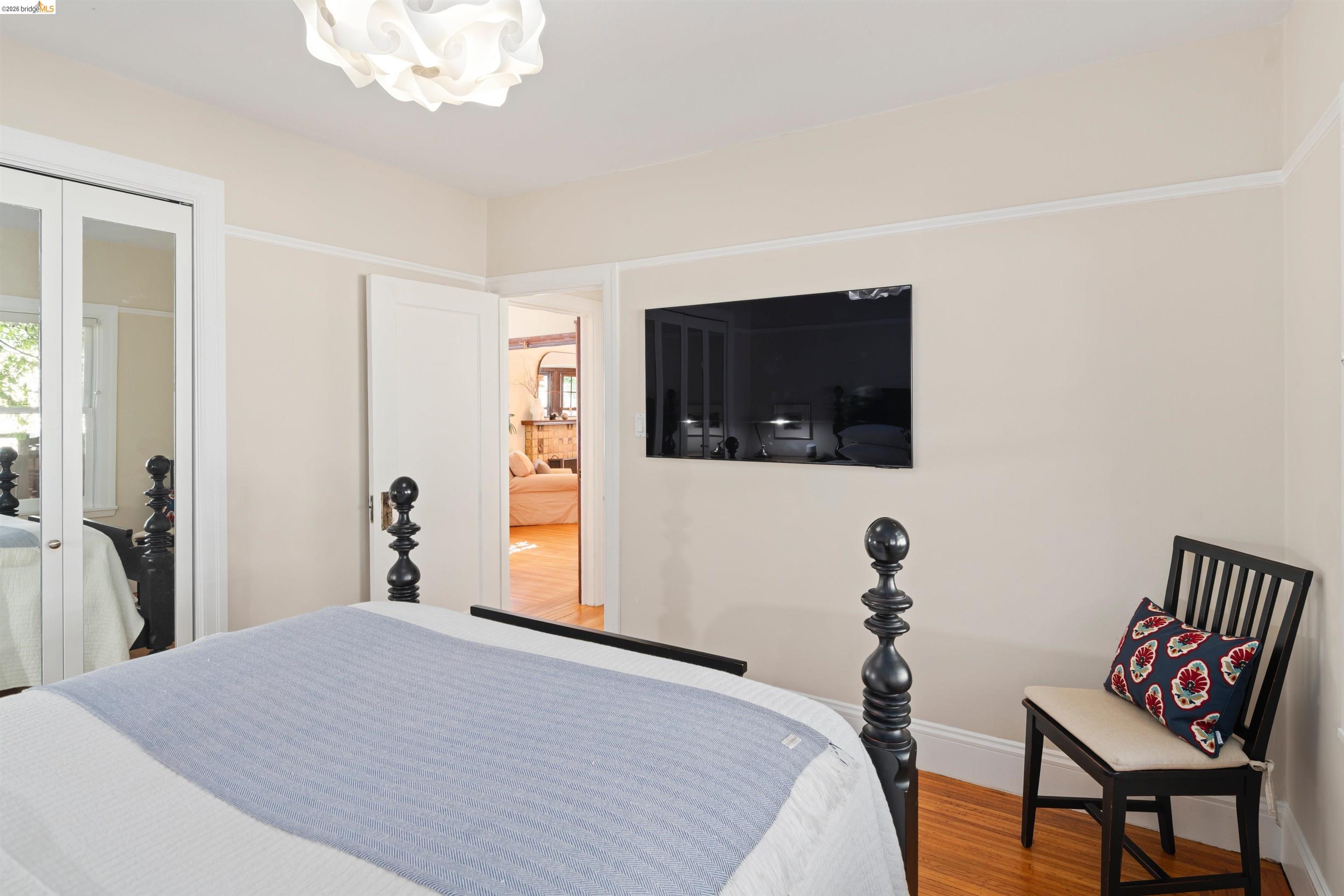 Furnished bedroom with mirrored closet doors, a wall-mounted television, and a black chair beside the bed.