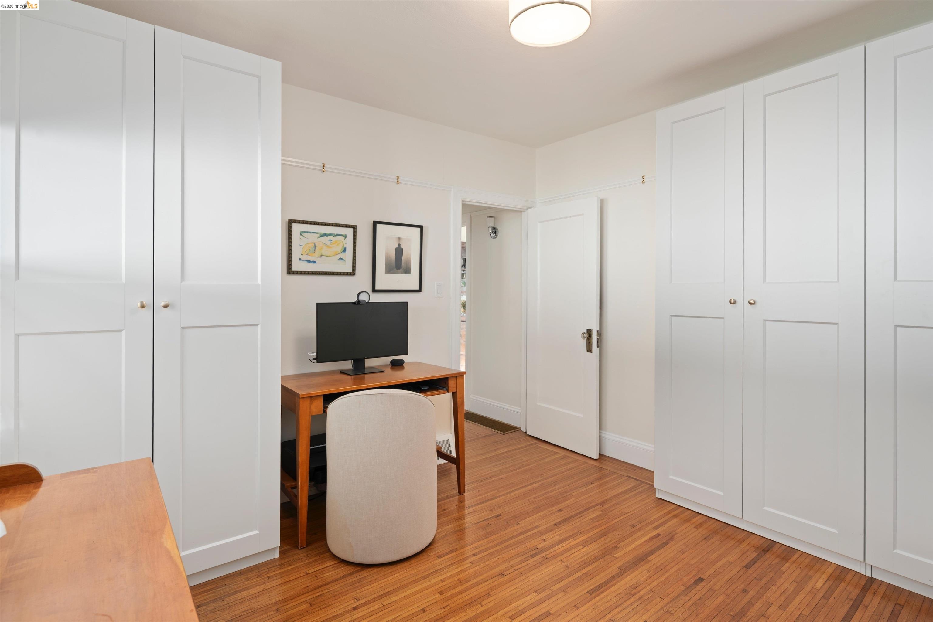 Home office with white built-in closets, a wooden desk, and hardwood floors.