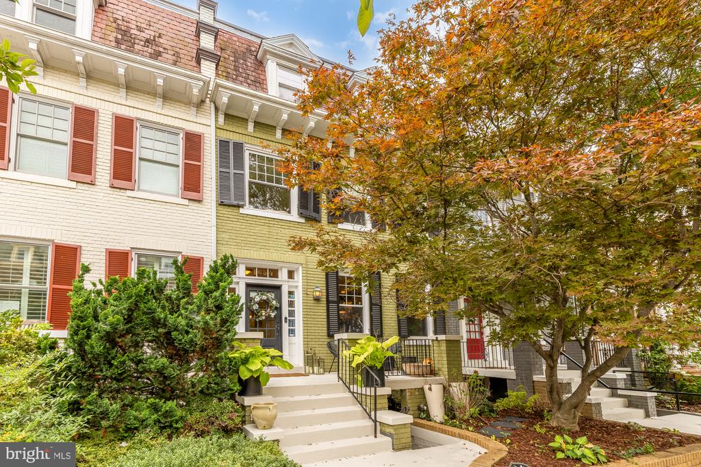 Pale green townhouse with black shutters, front steps, and autumn trees.