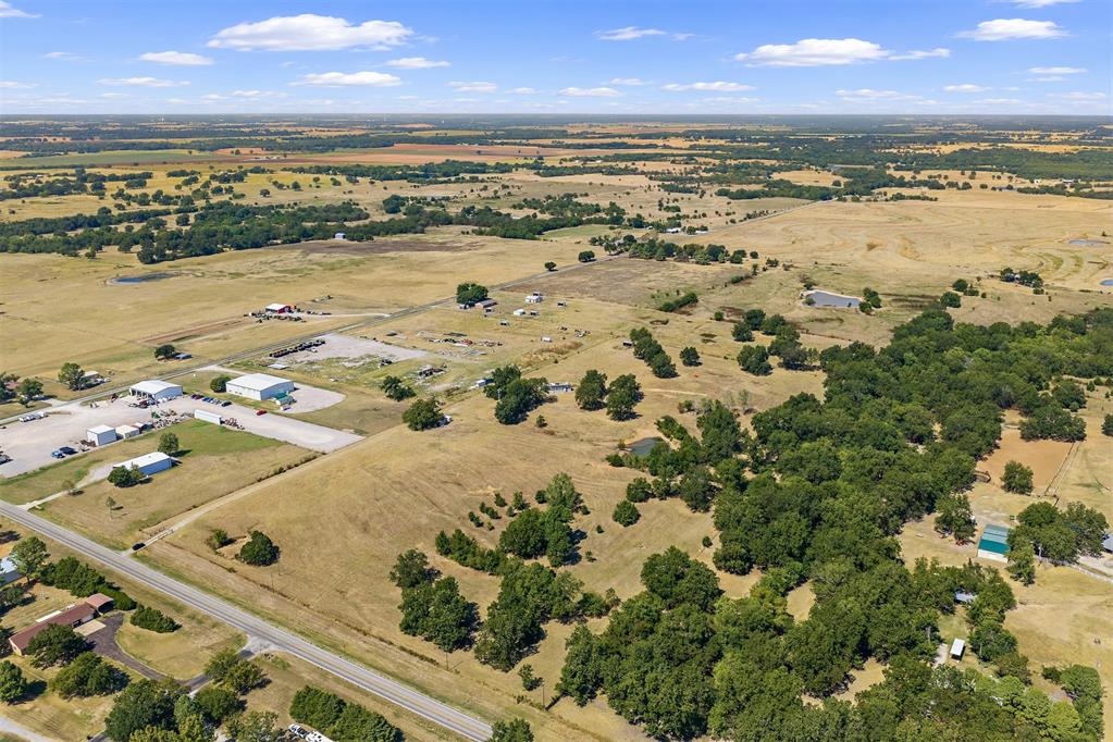 Aerial view of rural fields, scattered trees, small buildings, and roads.