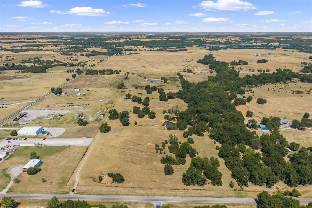 Aerial view of open fields and tree clusters, with buildings and a highway in the foreground.