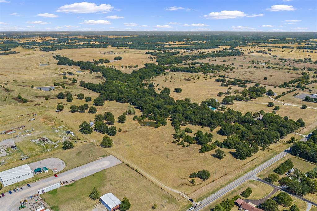 Aerial view of rural acreage with open fields, tree lines, and a highway along the foreground.