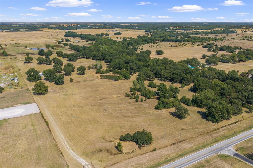 Aerial view of open pasture with scattered trees and highway frontage.