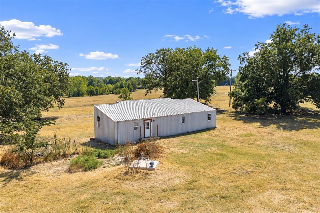 White metal building on open acreage, surrounded by mature trees and dry grass.