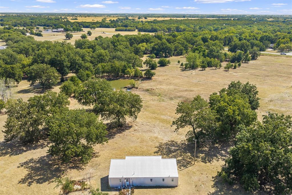 Aerial view of a small metal-sided building among scattered trees on open rural land.
