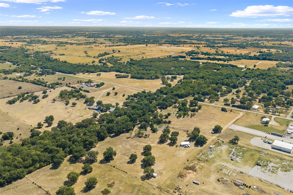 Aerial view of open pasture and wooded acreage with scattered buildings and rural roads.